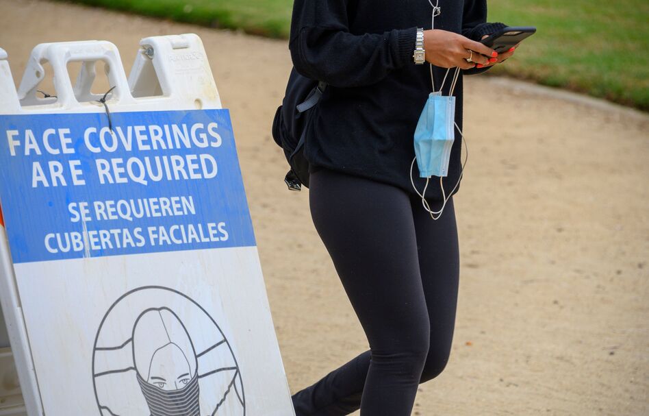 A woman carrying her mask walks past a sign mandating the wearing of face coverings in an effort to control the spread of coronavirus as she walks in Palisades Park in Santa Monica, Calif., on July 25, 2020. (Robyn Beck/AFP via Getty Images)