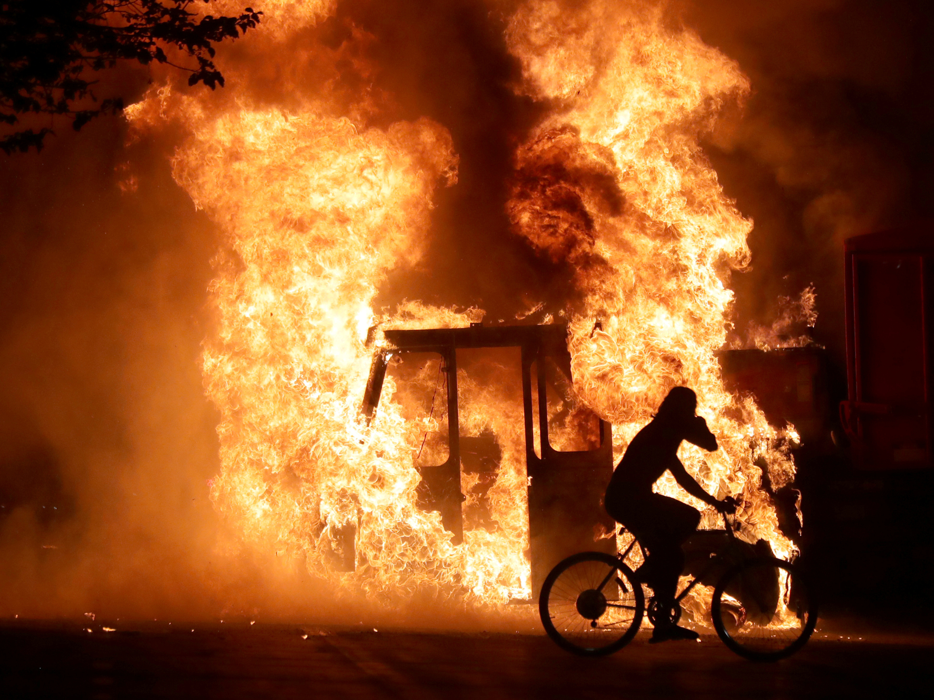 A man on a bike rides past a city truck on fire outside the Kenosha County Courthouse in Kenosha, Wis., during protests following the police shooting of Jacob Blake, a Black man, on Sunday. (Via Reuters)