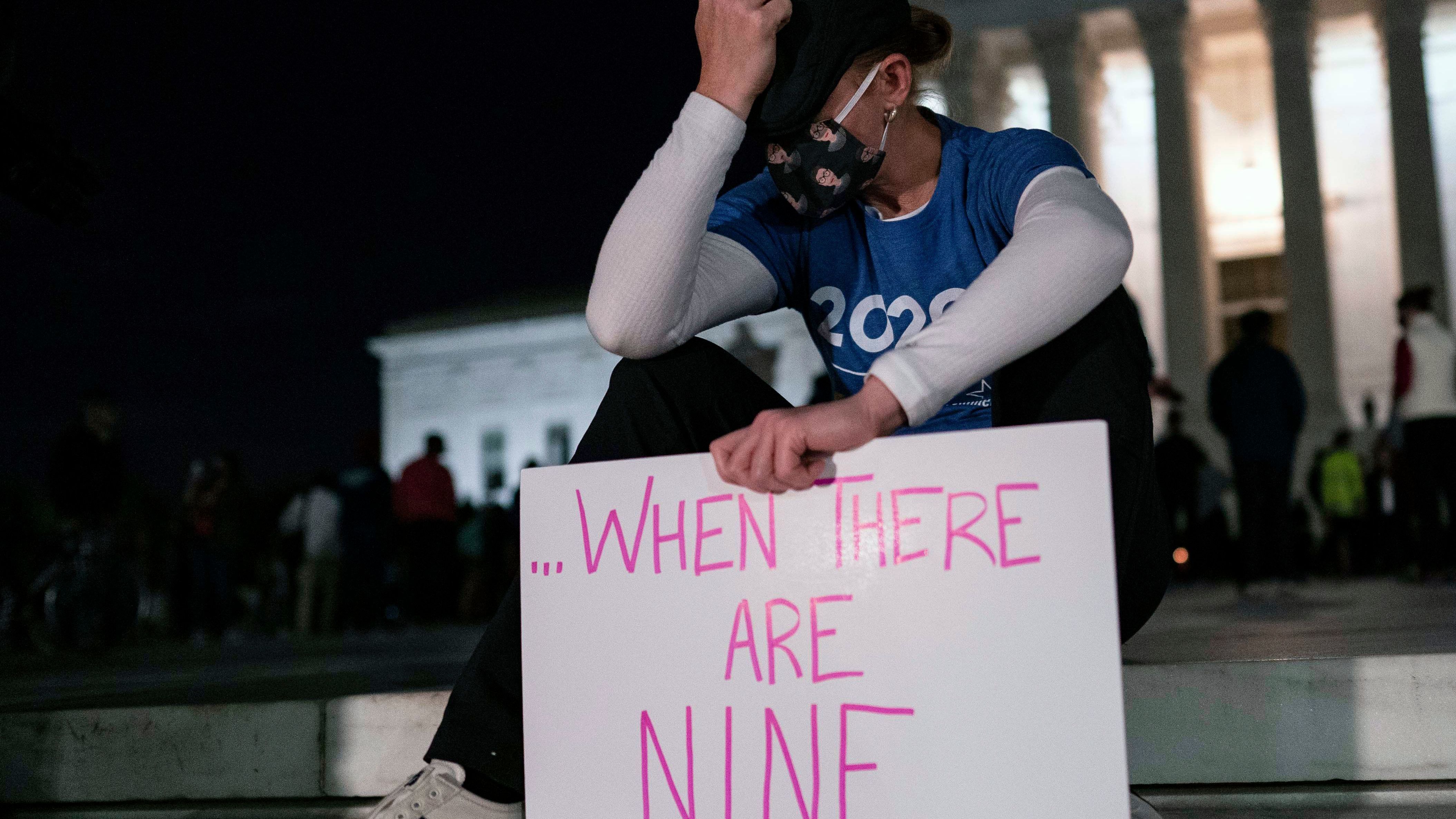 A woman, mourning the death of Ruth Bader Ginsburg, holds a sign at the Supreme Court that reads, "when there are nine," something Ginsburg said to describe when there