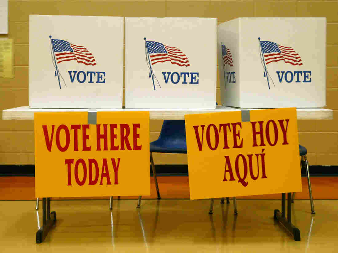 Signs in English and Spanish encourage voters to cast their paper ballots. Above the signs are three cardboard polling stations. (Photo by Steven Clevenger/Corbis via Getty Images)