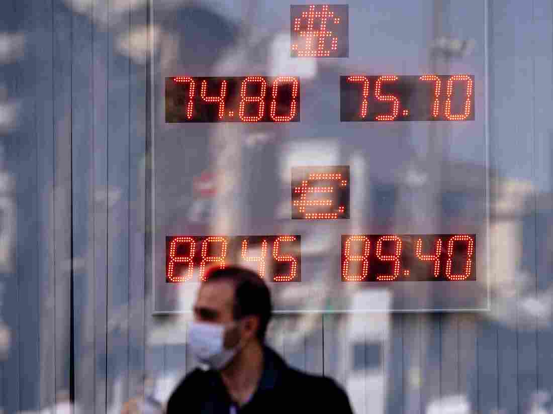 A man wearing a face mask passes by a screen displaying the currency exchange rate of the Russian ruble with U.S. dollar and Euro, September 2020.