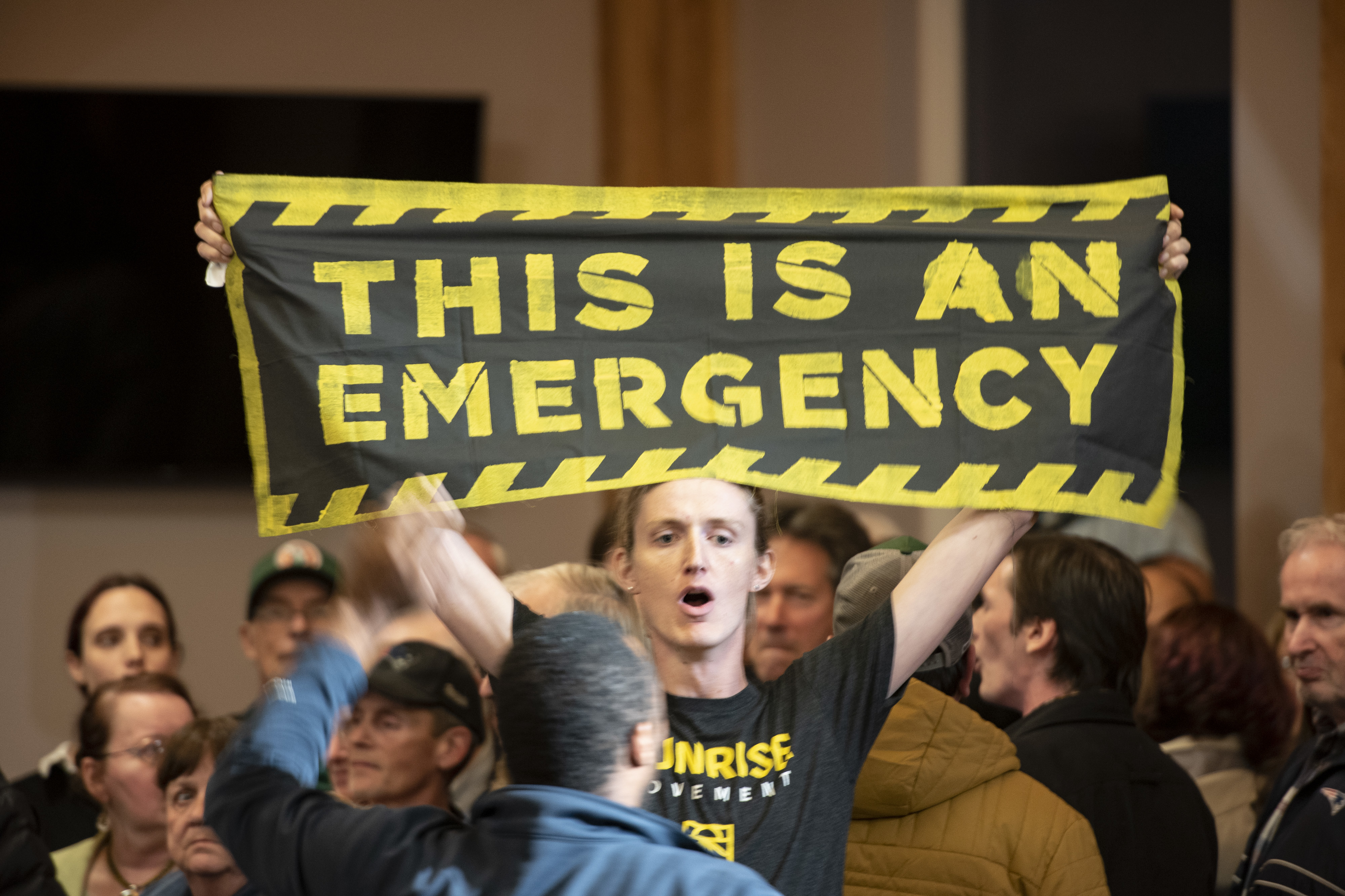 A climate change protester holds a banner reading, &quot;This Is An Emergency,&quot; during a 2019 town hall event in Manchester, N.H., with Joe Biden, who isn't pictured. (Bloomberg via Getty Images)