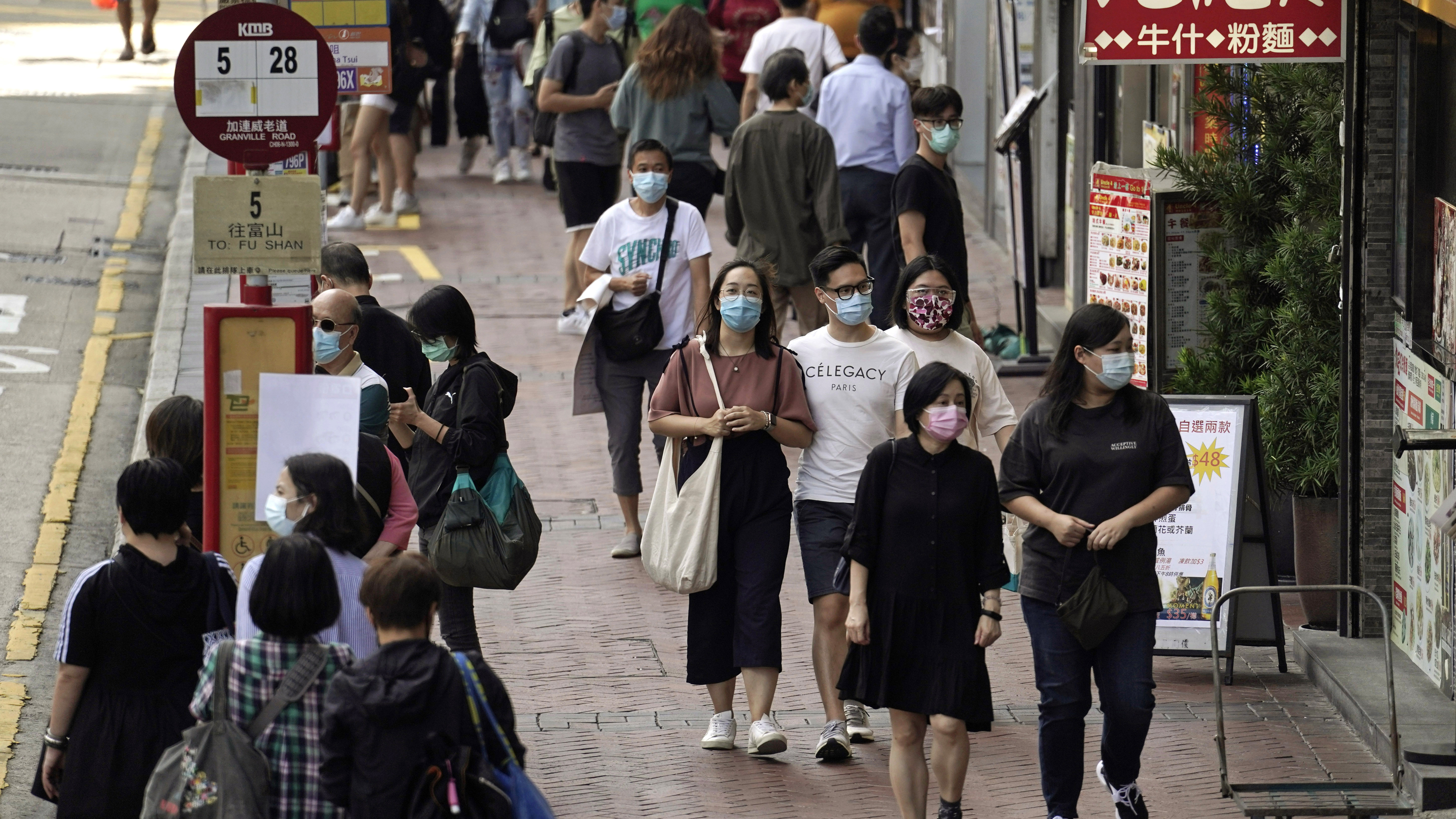 In this Oct. 9, 2020, photo, people walk down a street in Hong Kong. Singapore and Hong Kong have postponed a planned air travel bubble meant to boost tourism amid a spike in coronavirus infections in Hong Kong.