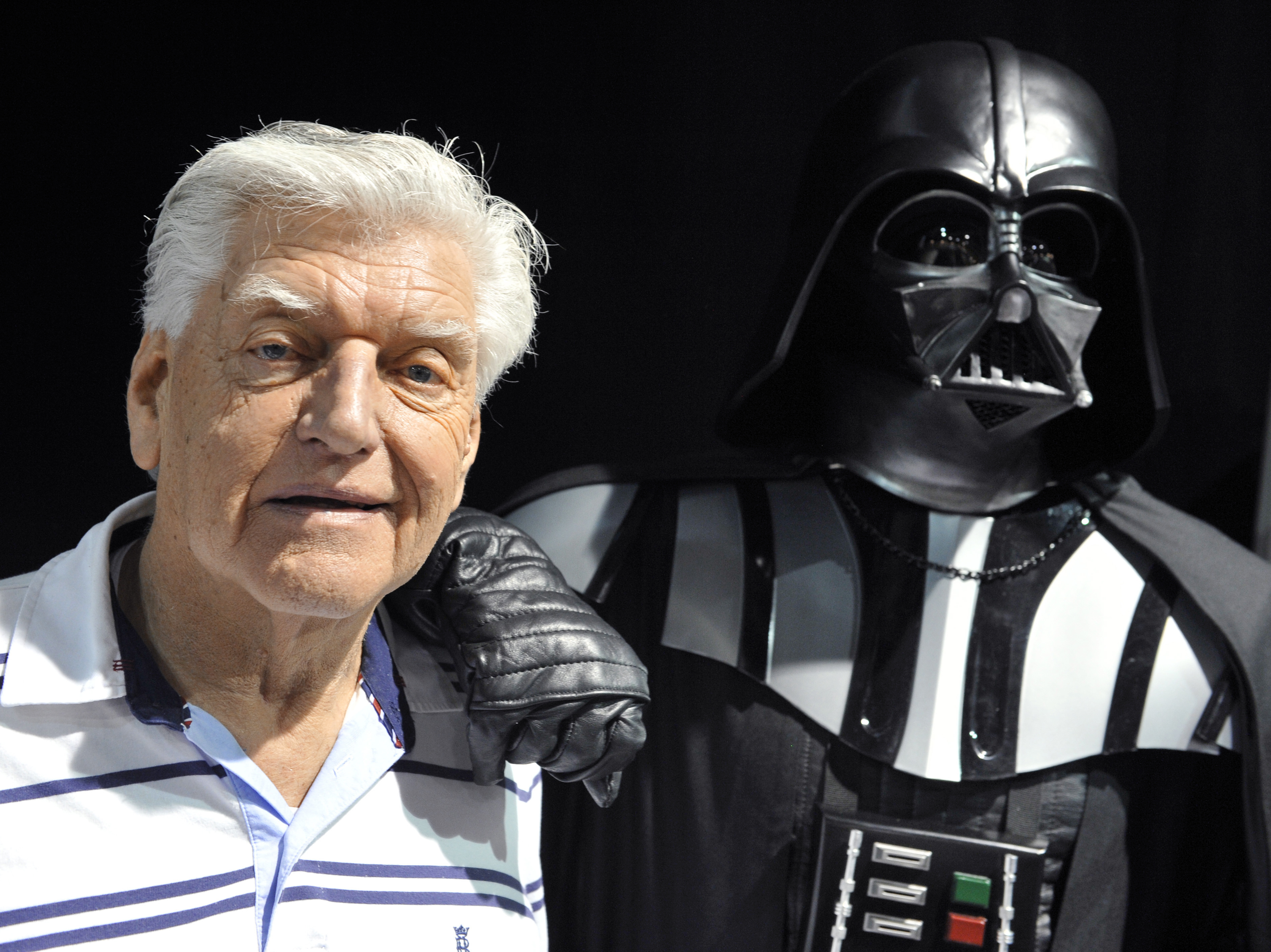 British actor David Prowse, who played Darth Vader in the first Star Wars trilogy, poses with a fan dressed in a Darth Vader costume during a Star Wars convention on April 27, 2013. On Sunday morning, Prowse's management company shared the news of his death at age 85. (AFP via Getty Images)