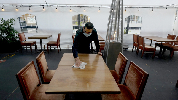 A person cleans a table in an outdoor tented dining area of a restaurant in Sacramento, Calif., on Nov. 19. Job growth slowed sharply in November as relief aid is due to expire at the end of the year.