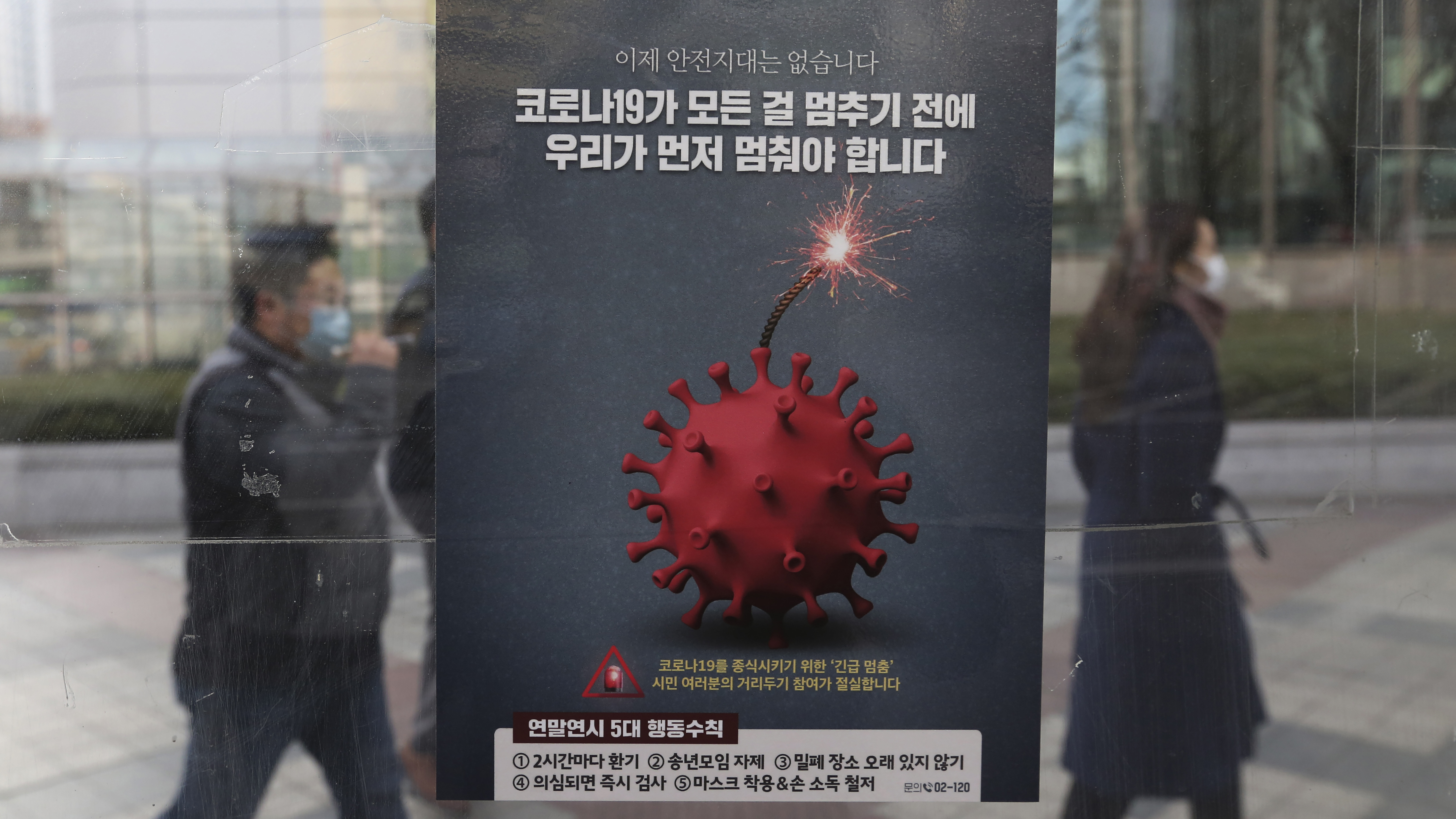 People wearing face masks as a precaution against the coronavirus pass by a poster emphasizing an enhanced social distancing campaign at a bus station on Monday in Seoul, South Korea.