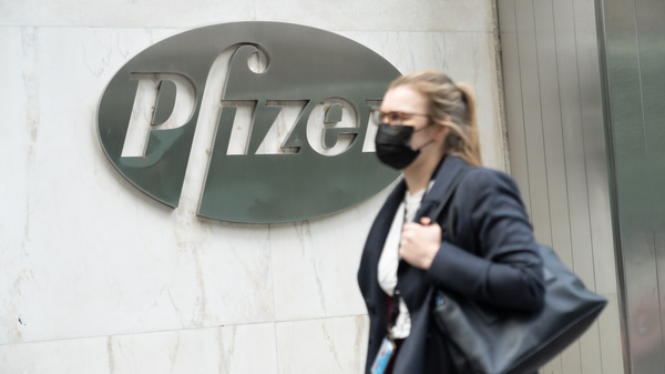 A woman wearing a face mask walks past a Pfizer