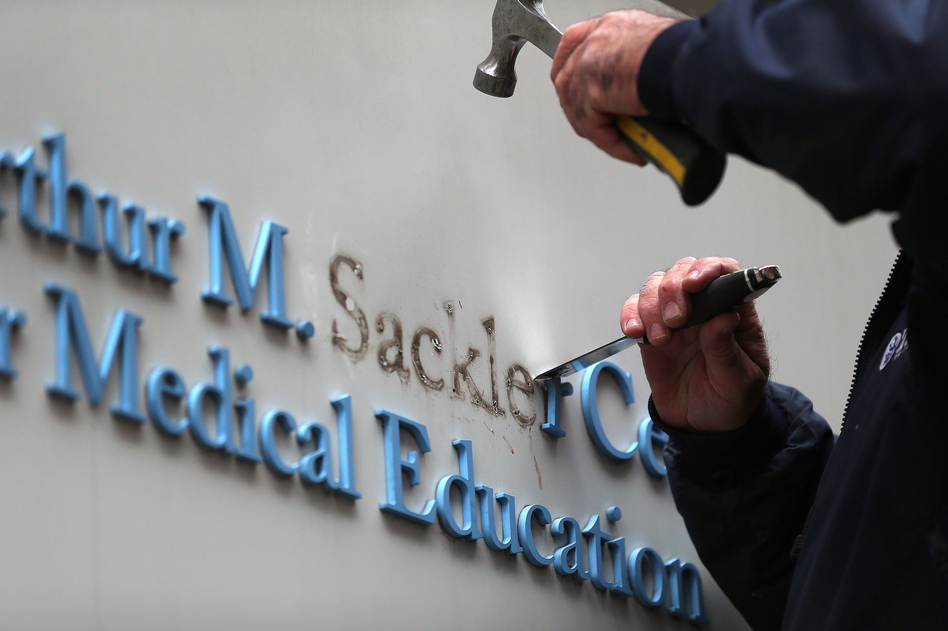 Tufts employee Gabe Ryan removes the Sackler family name from a building at Tufts University, the first major university to strip the Sackler name from buildings and programs. (Boston Globe via Getty Images)