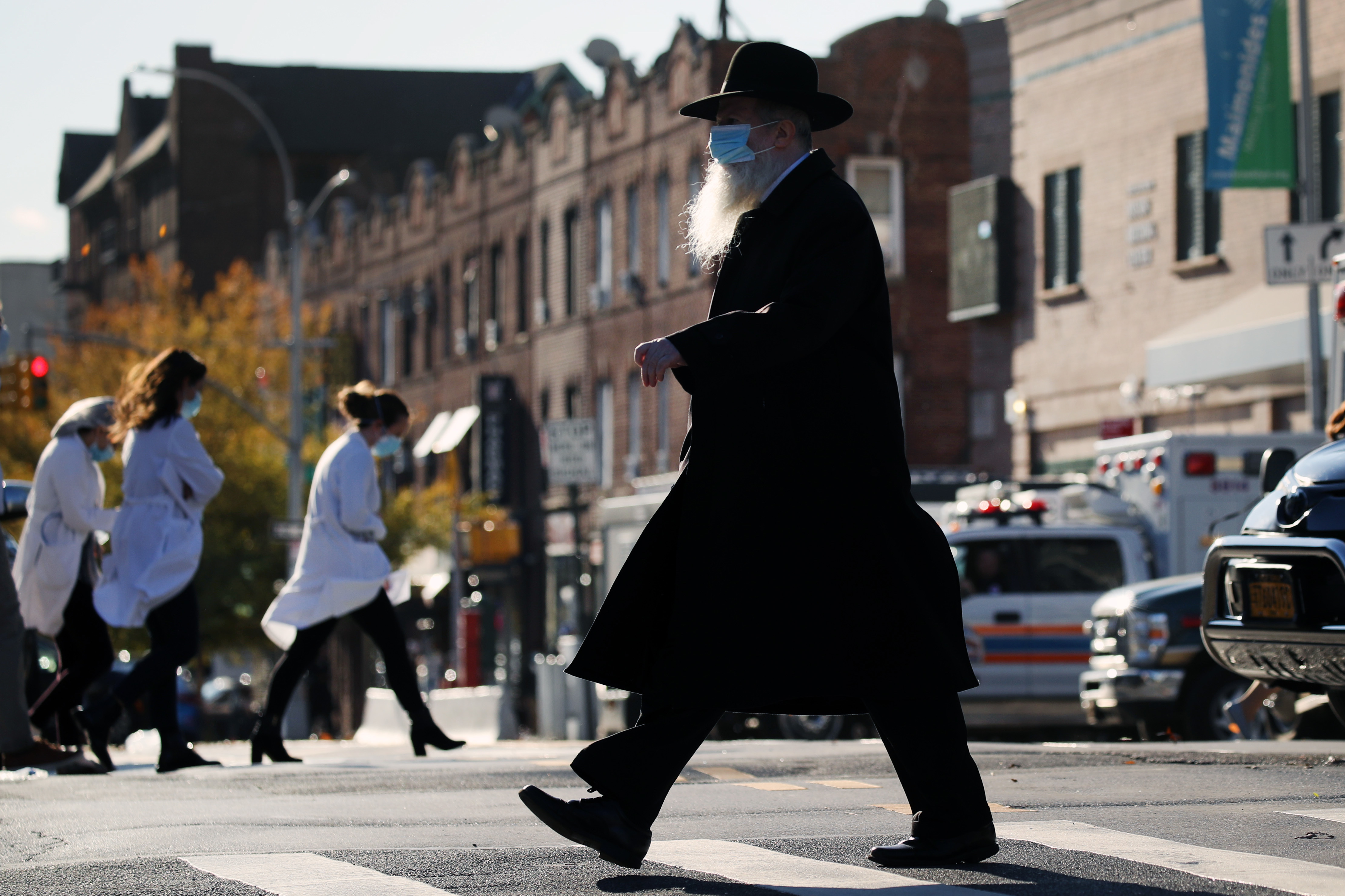 A Hasidic man and medical workers cross paths near the Maimonides Medical Center in Brooklyn, N.Y., in November. When public health messaging comes from community leaders, it's much more likely to be adopted, research on diverse groups finds. (Getty Images)