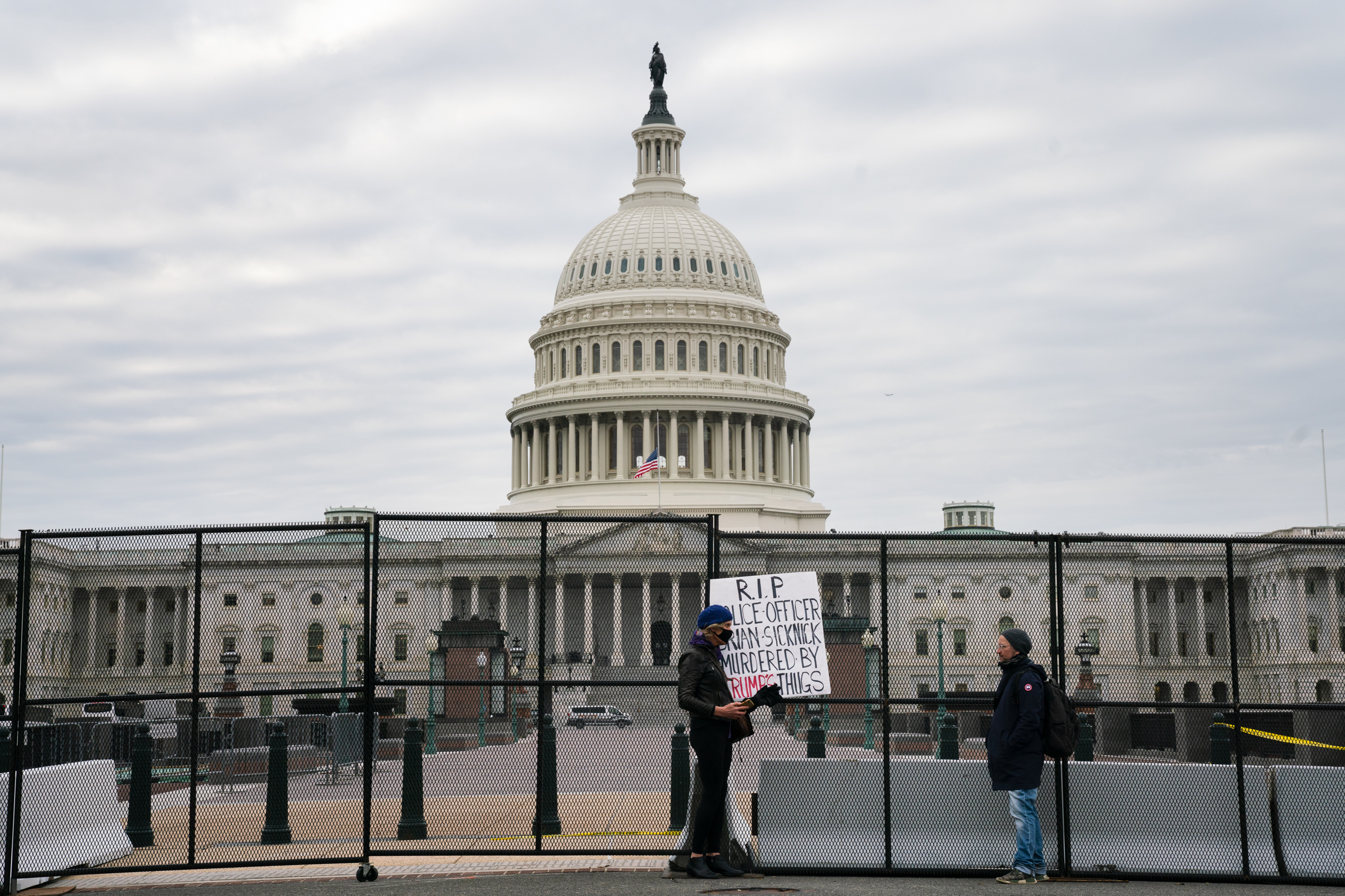 A person outside the U.S. Capitol holds a sign for U.S. Capitol Police officer Brian Sicknick who died from injuries he sustained during the siege on the Capitol by pro-Trump extremists. (NPR)