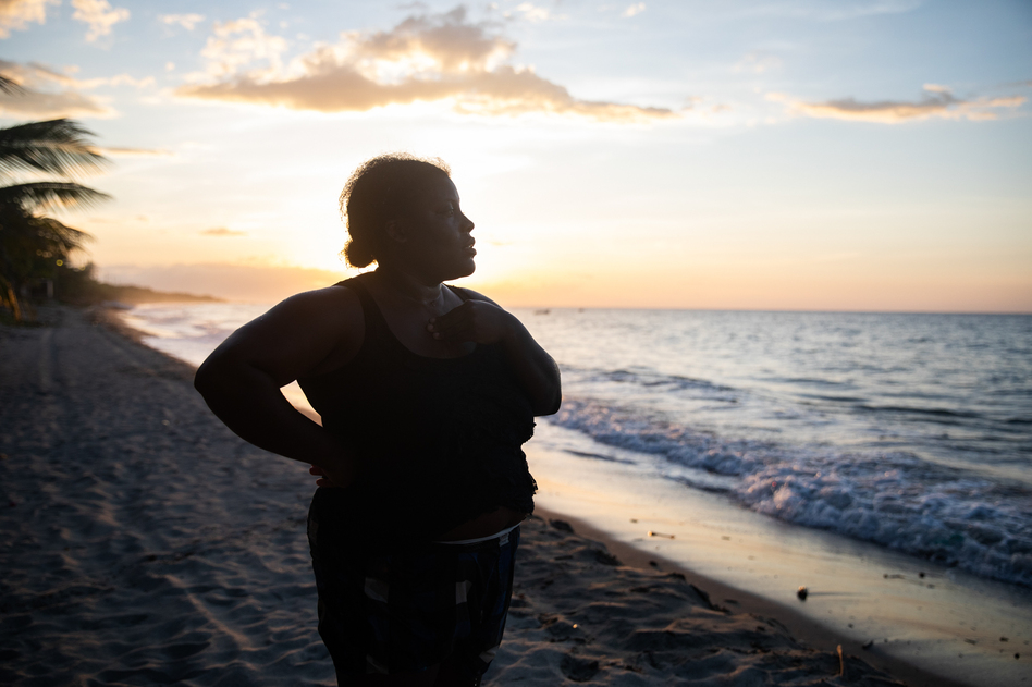 With the sun setting off the coast of northern Honduras, Ella Guity watches her daughters, Jirian and Eleny, swim in the warm Caribbean waters of the village of Rio Esteban, home to a group with African and indigenous roots known as the Garifuna. Ella had left years earlier for life in the big city, but the pandemic led her back home. (Tomas Ayuso for NPR)