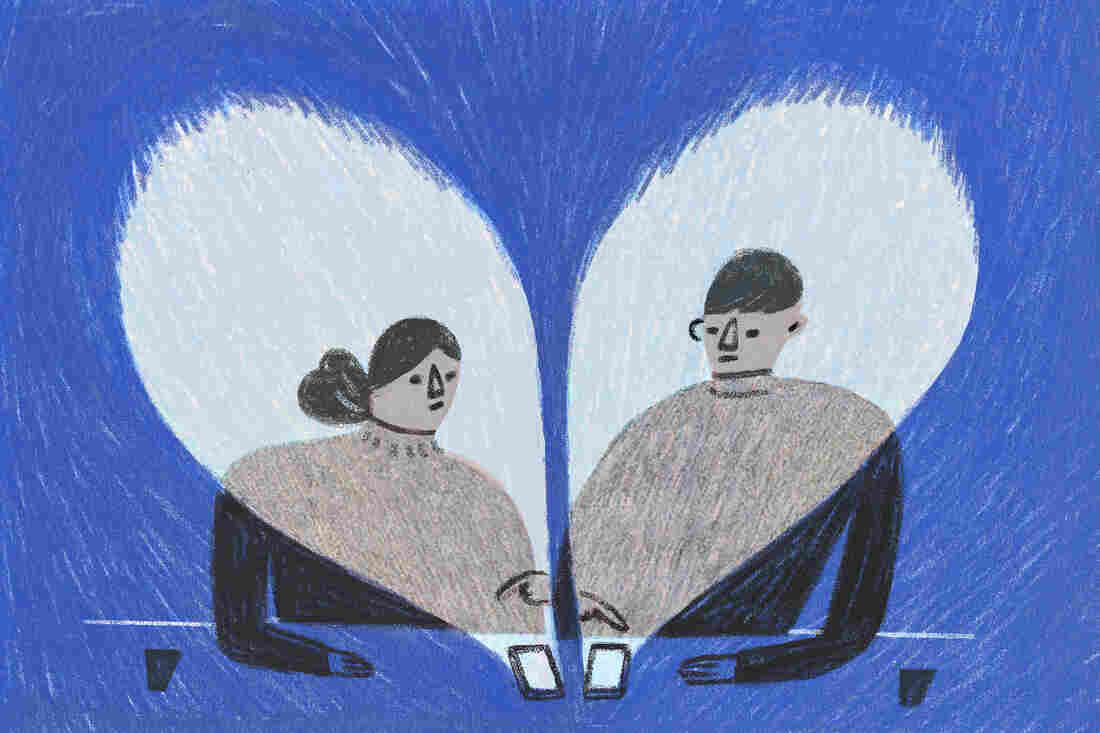 Two people sit next to each other swiping on their phones.