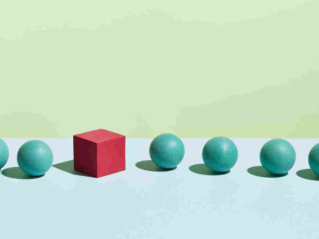 A red cube stands in a row of green spheres