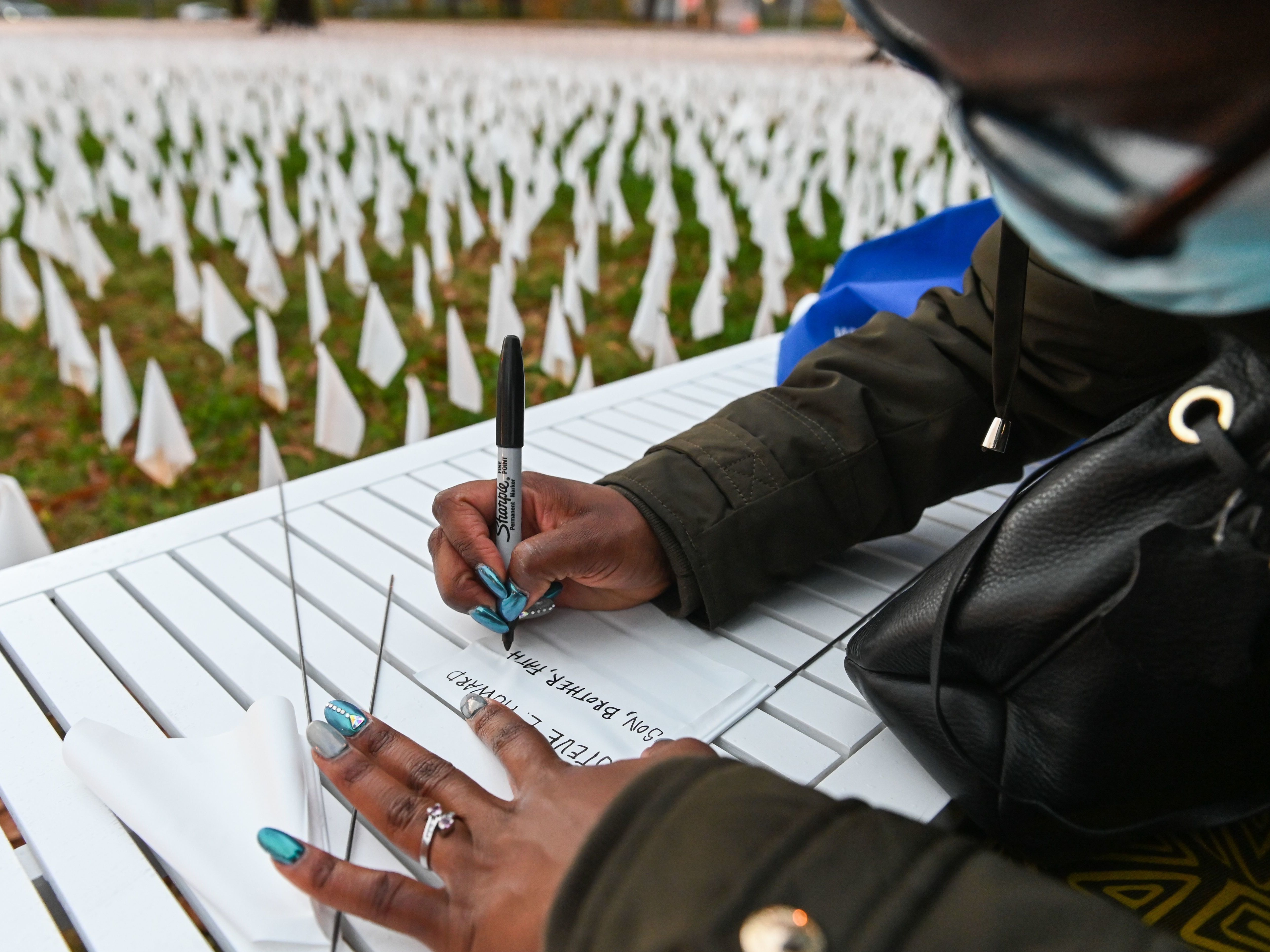 Patrice Howard writes on white flags before planting them to remember her recently deceased father and close friends in November at &quot;IN AMERICA How Could This Happen...,&quot; a public art installation in Washington, D.C. Led by artist Suzanne Firstenberg, volunteers planted white flags in a field to symbolize each life lost to COVID-19 in the U.S. (AFP via Getty Images)