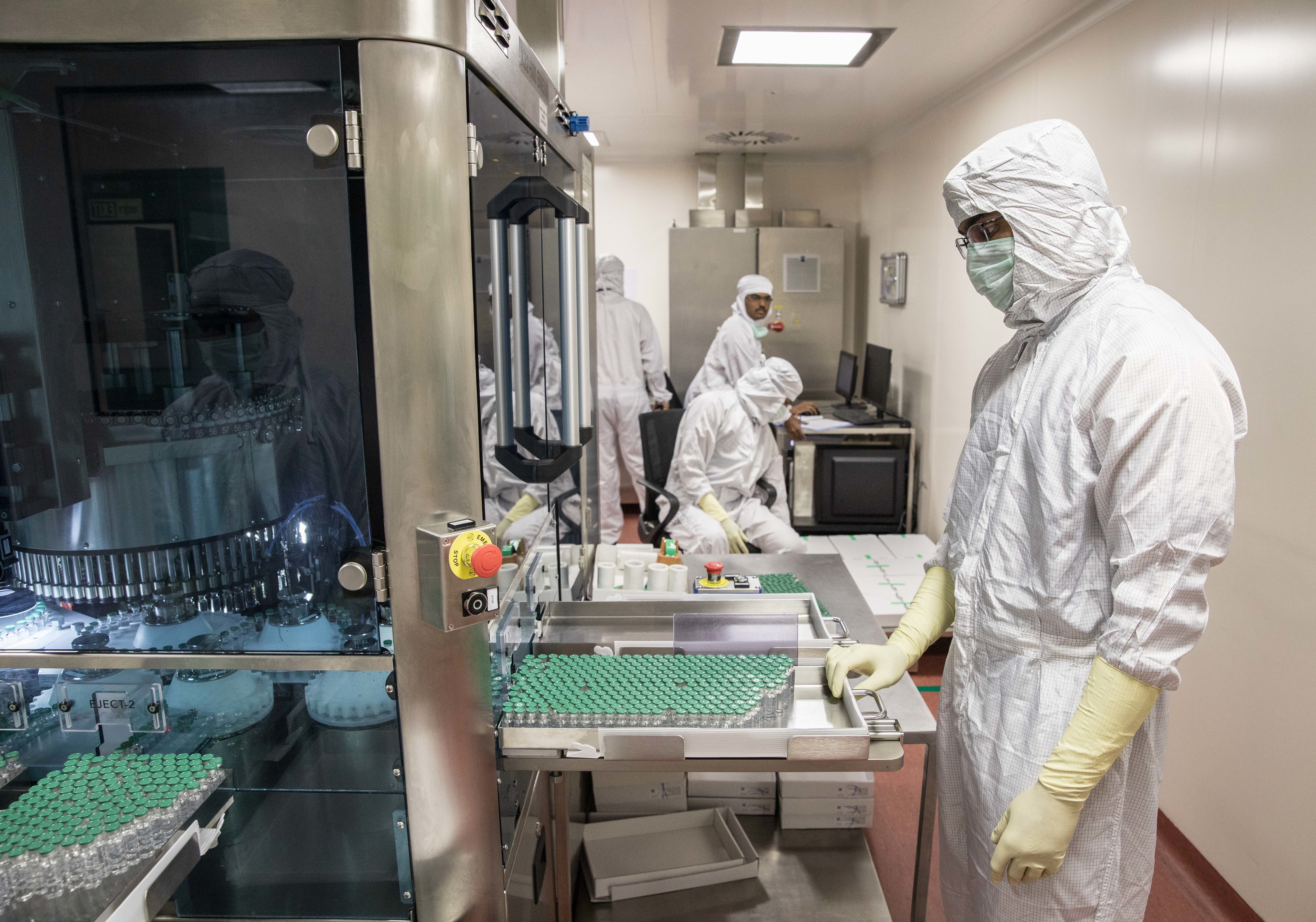A technician waits to collect vials containing vaccine after they pass through a machine that checks for bottling and vaccine substance deficiencies. (Viraj Nayar for NPR)