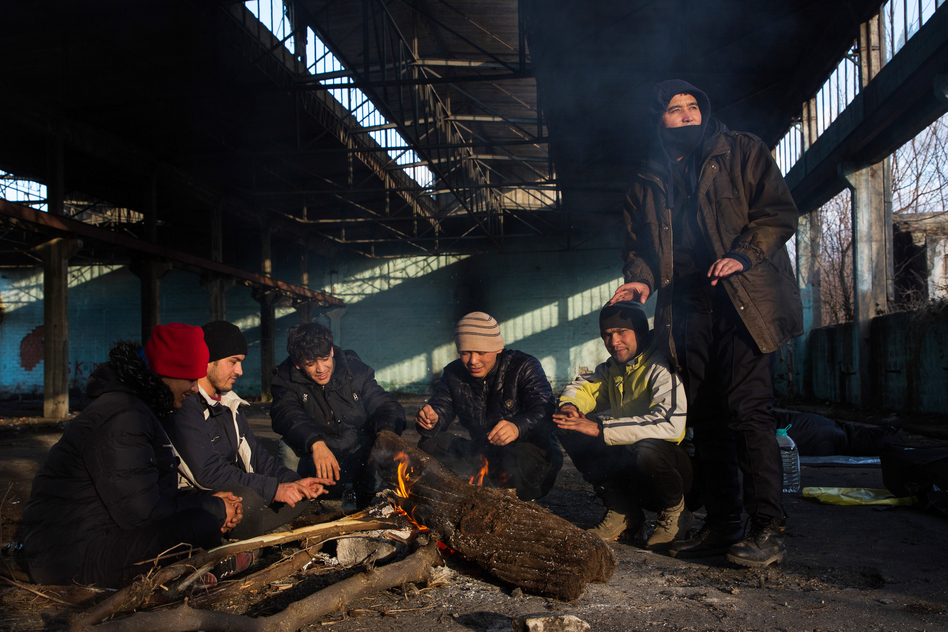 Afghan Morteza Mohammadi (center-left) and his companions sit around a fire in the former Krajina Metal factory in Bihac, Bosnia-Herzegovina, near the Croatian border, discussing possible border crossing strategies related to the weather and time. (Elisa Oddone)