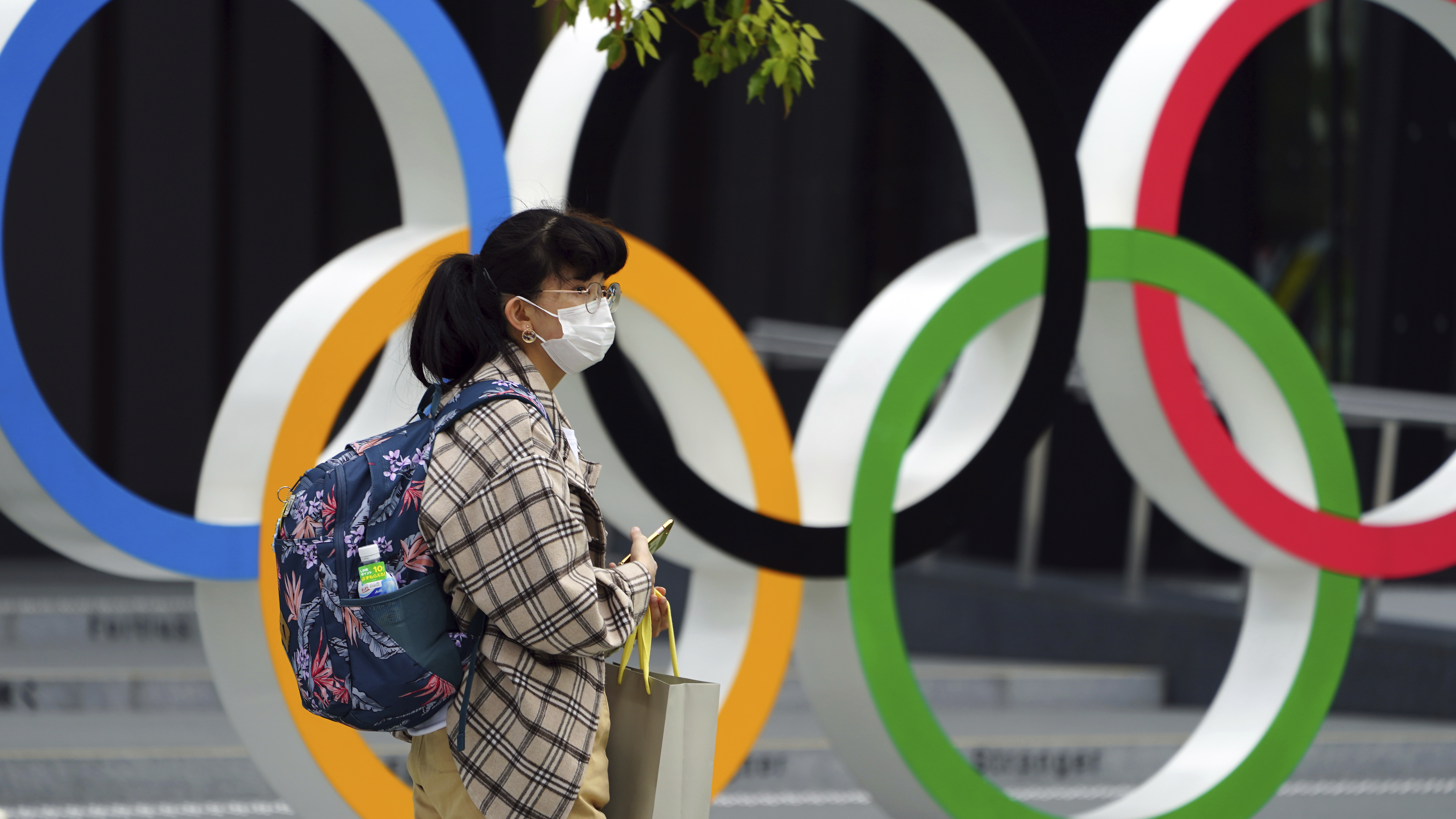 A woman wearing a protective mask to help curb the spread of the coronavirus walks in front of he Olympic Rings on Tuesday in Tokyo. North Korea says it will not attend the games over COVID-19 fears.