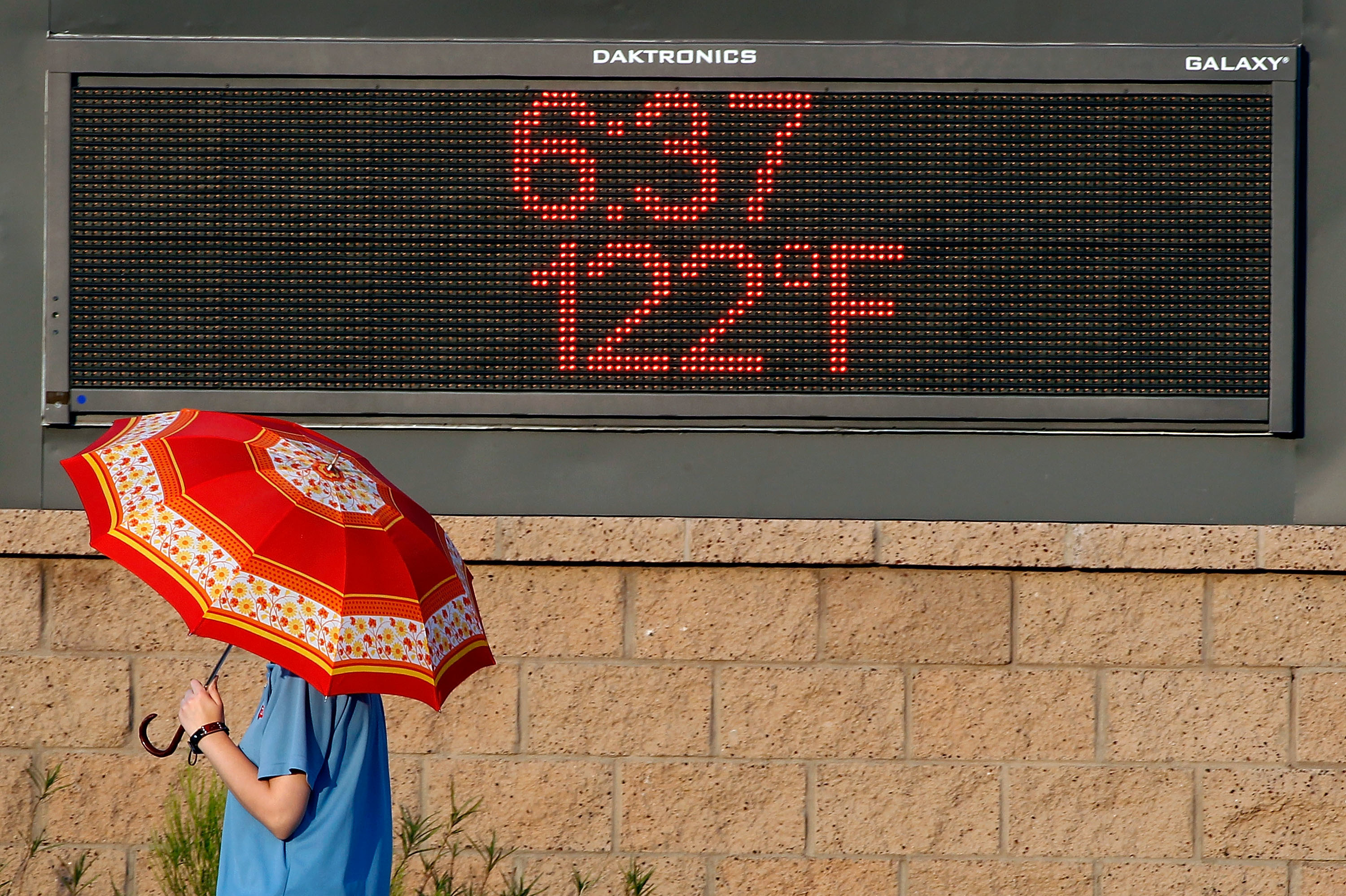 A pedestrian using an umbrella to get some relief from the sun walks past a sign displaying the temperature on June 20, 2017, in Phoenix. (Getty Images)