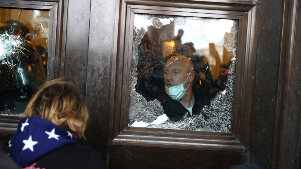 A Capitol police officer looks out of a broken window as pro-Trump rioters storm into the building on Jan. 6. (Getty Images)