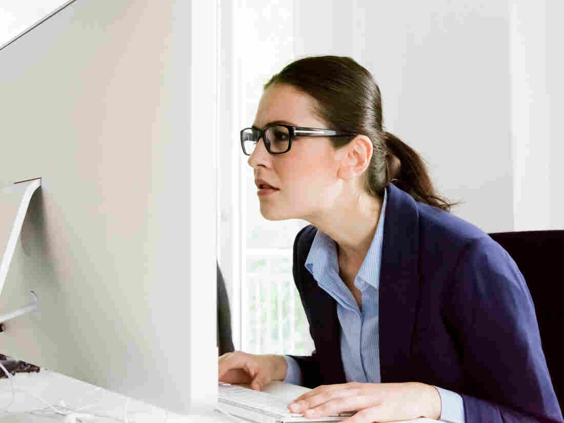 Confused young businesswoman can`t believe what she is reading on her computer screen. Sitting close to the screen trying to understand. Natural Office interior light.