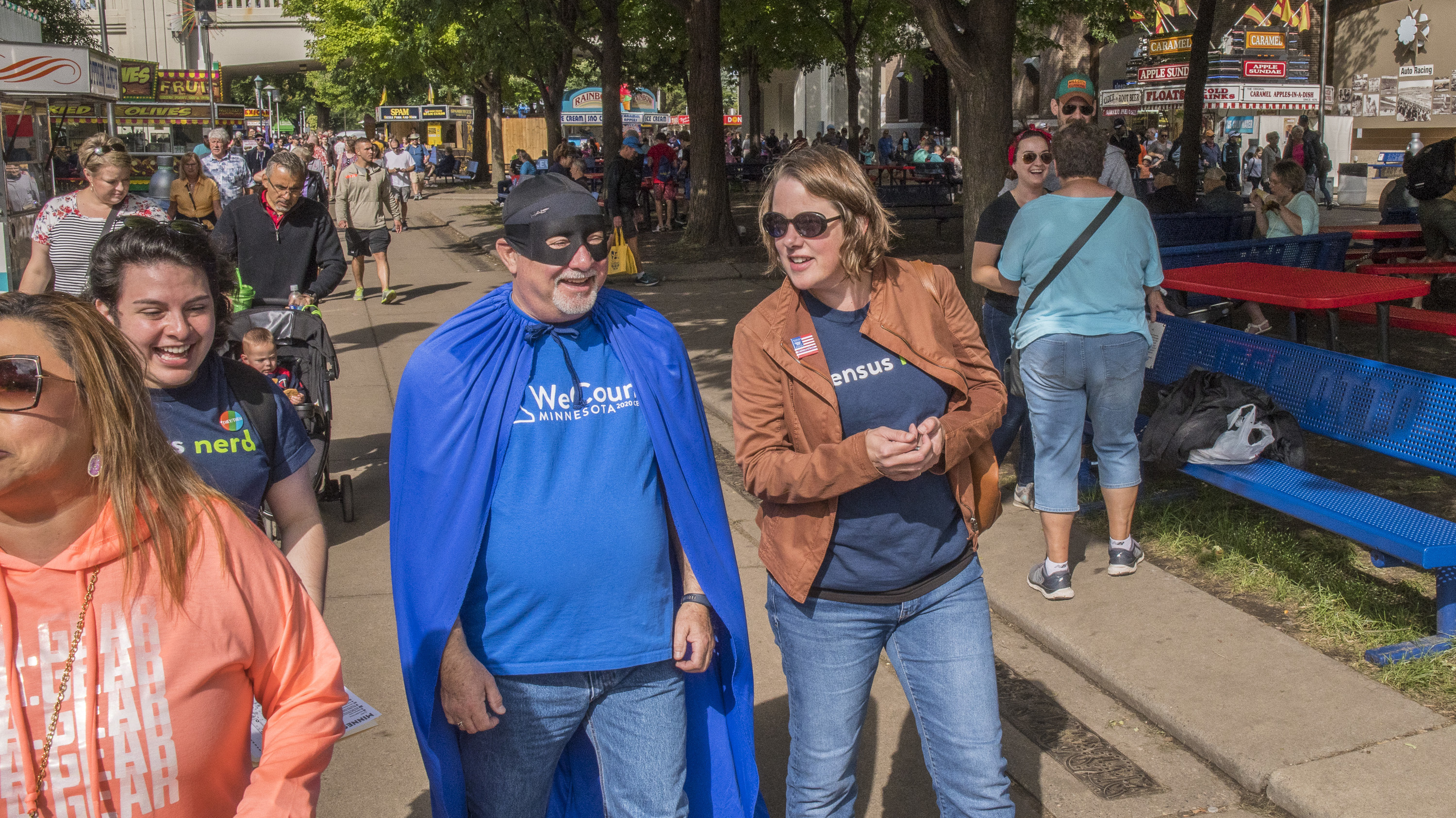 Minnesota's state demographer, Susan Brower (center), walks with Dean Goldberg, donning a blue cape and black mask as &quot;Census Man,&quot; through the 2019 Minnesota State Fair in St. Paul, Minn., to encourage residents to participate in the national head count. (Minnesota Department of Administration)