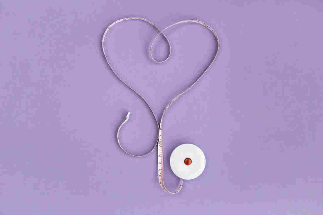 A measuring tape is arranged in a heart shape on a light purple background.