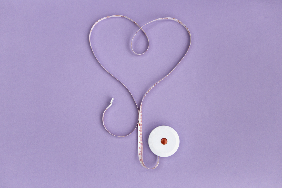A measuring tape is arranged in a heart shape on a light purple background.