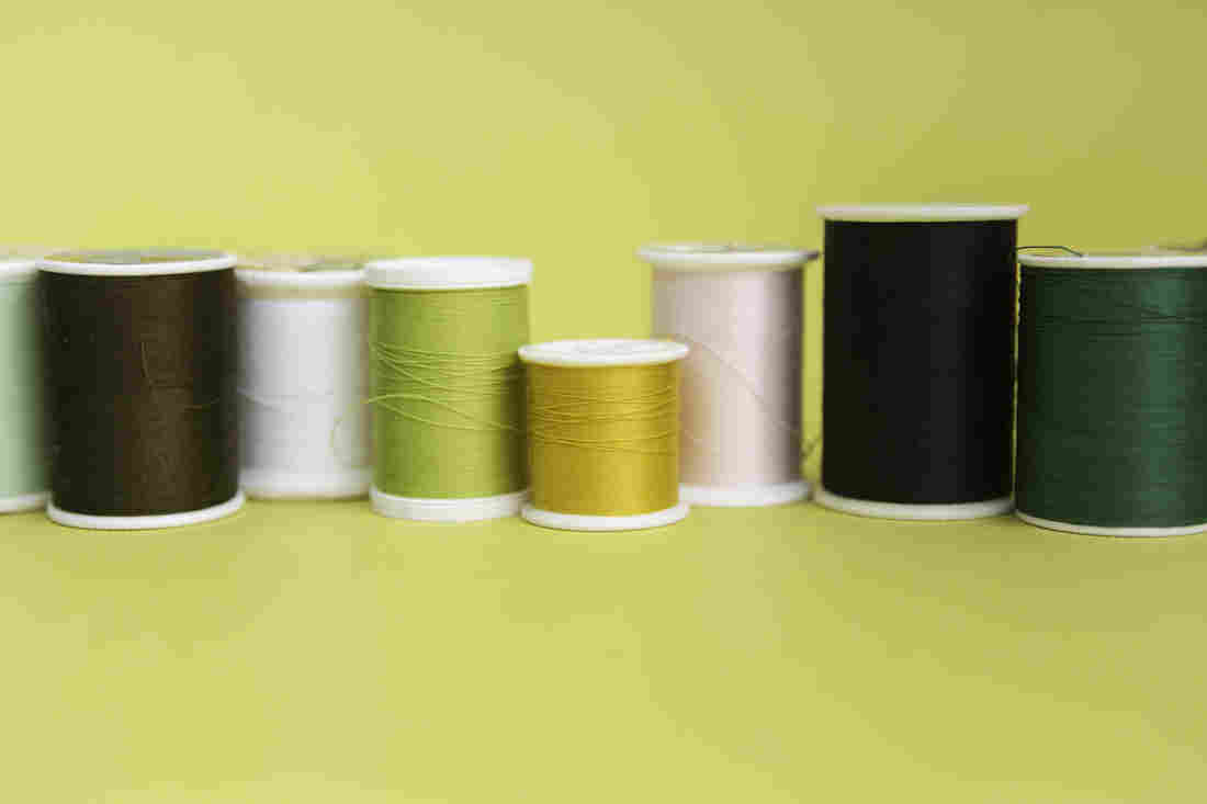 Spools of thread of varying colors are lined up in a loose row against a light yellow backdrop.