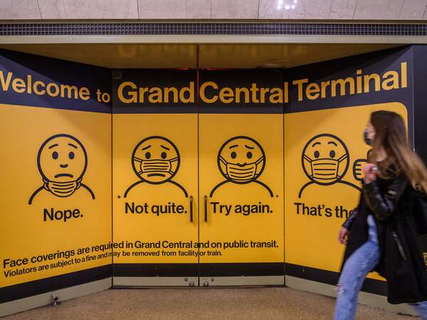 A woman walks past posters explaining mask requirements at Grand Central Terminal train station in New York City on Wednesday. Rules requiring masks on transit are unchanged by the Centers for Disease Control and Prevention's updated mask guidance for fully vaccinated people.