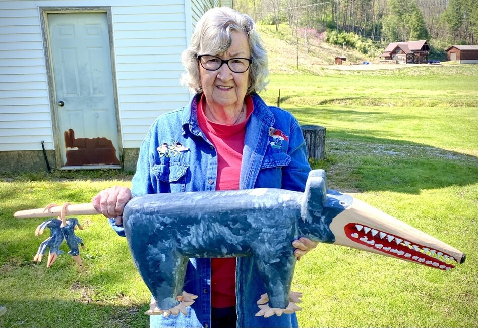 Minnie Adkins stands in her yard in Elliott County, Ky., holding her carving of a possum with baby possums dangling on its tail.