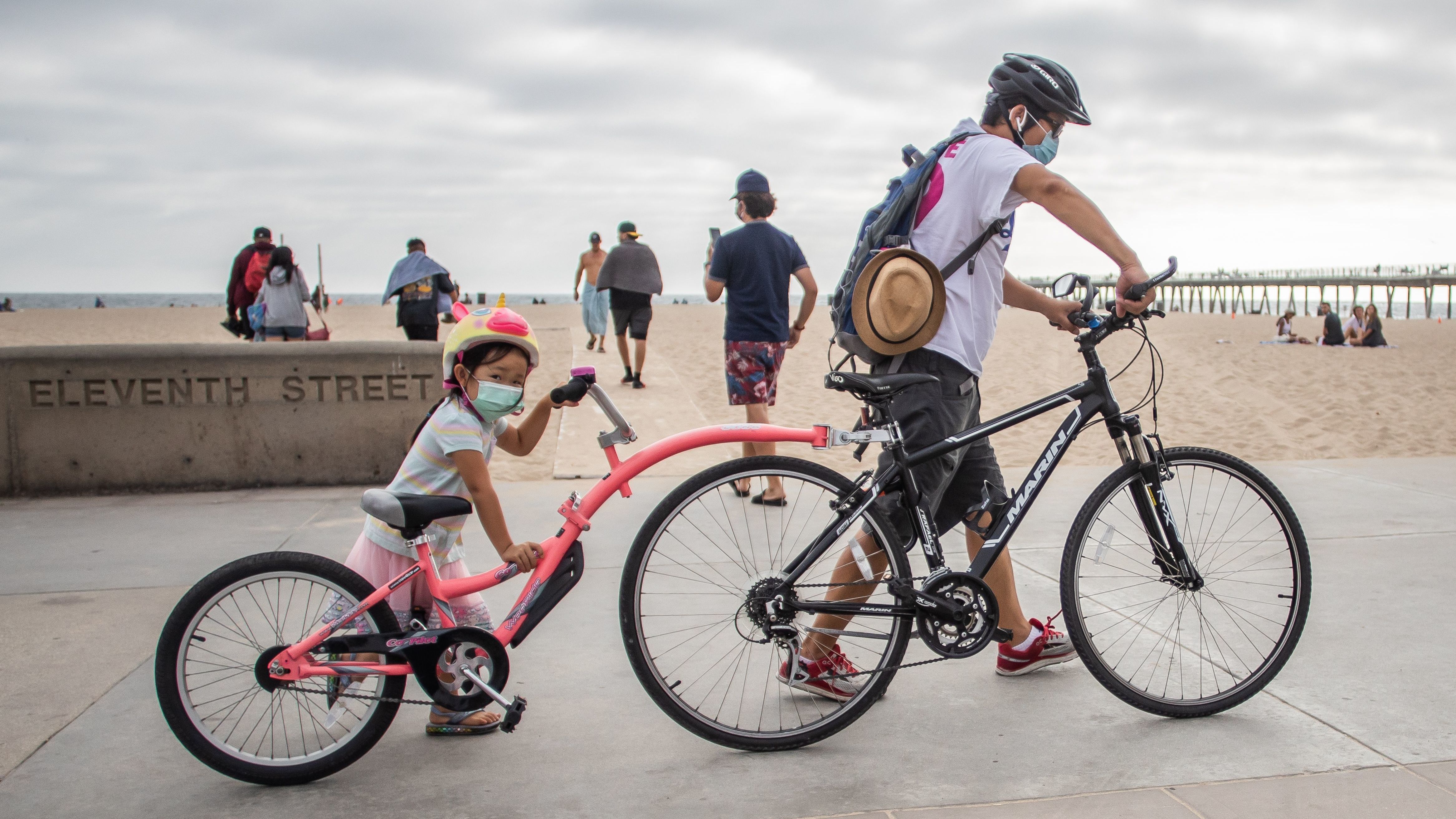 A girl and her father wear face masks while they push their bikes last summer in Hermosa Beach in the Los Angeles area. There aren