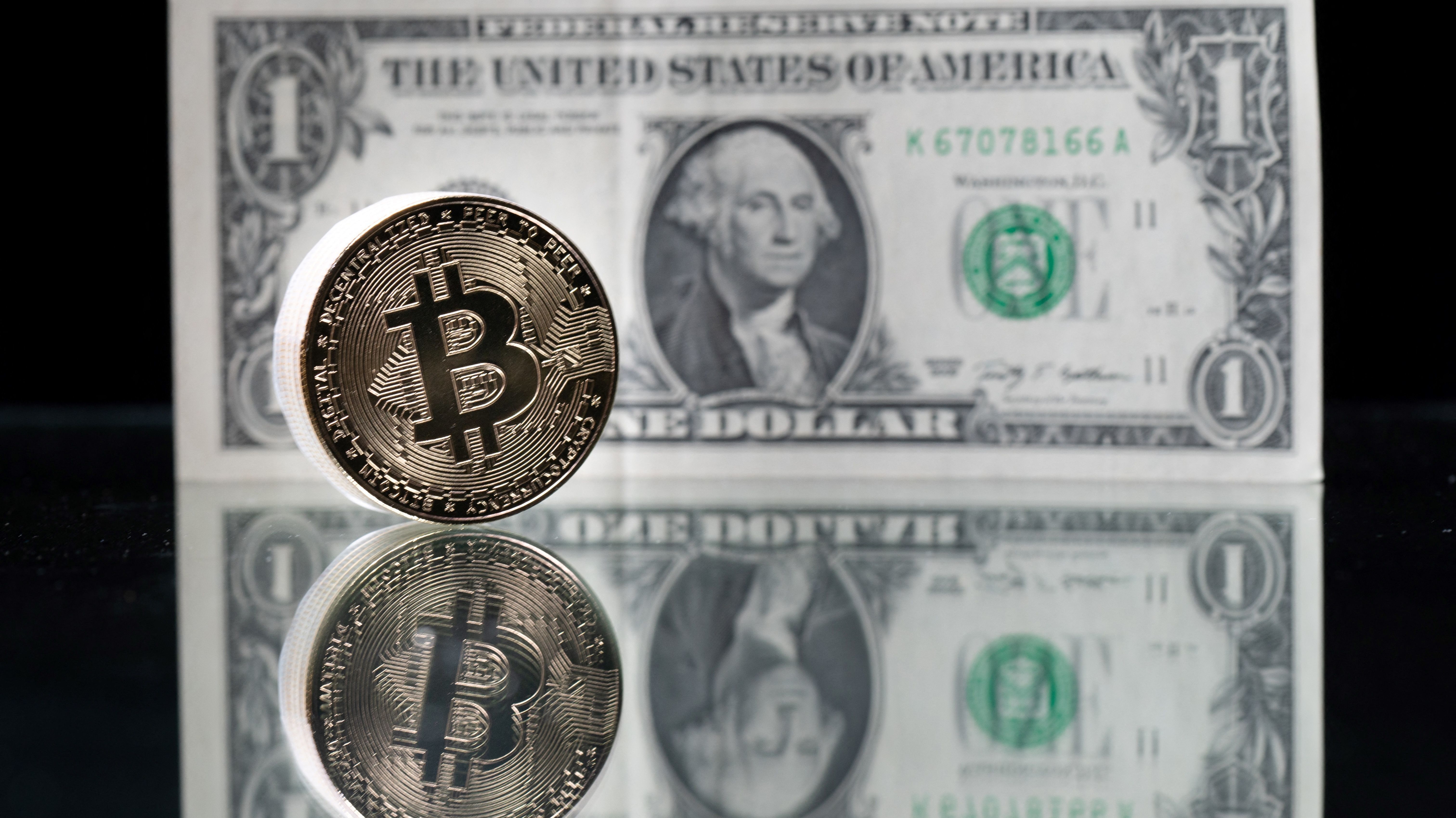 A physical imitation of the Bitcoin cryptocurrency is pictured with a $1 bank note. Cryptocurrencies are plunging over a range of factors, including the spillover impact from falling stock markets and fears about increased regulations.
