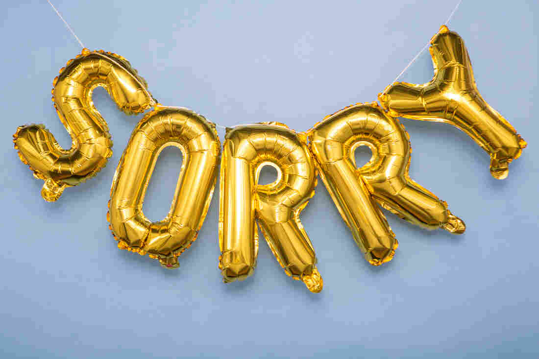 Gold foil balloons spelling the word "sorry" are strung up in front of a blue backdrop.