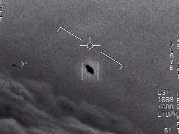 In an image from video footage from 2015, an unexplained object is seen at center as it soars among the clouds, traveling against the wind. "There's a whole fleet of them," a naval aviator tells another, though only one indistinct object is shown.