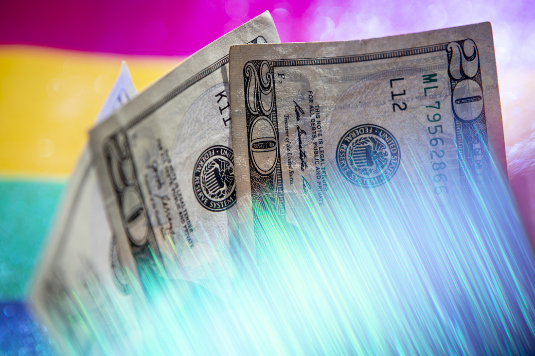 A photograph of three twenty dollar bills in front of bright, striped background. A prism warps the bottom of the money with glowing streaks in the bottom of the frame.