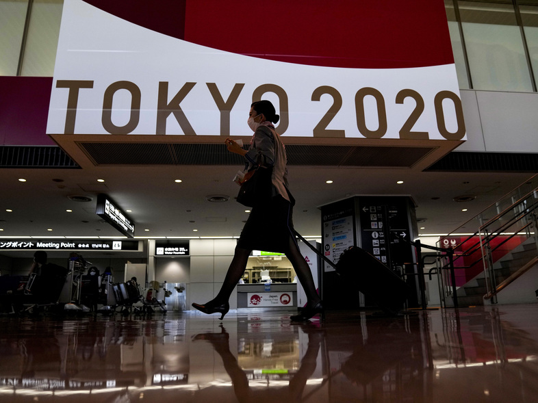 A flight attendant walks by a large display of Tokyo 2020 Olympics at Narita International Airport on Thursday in Narita, east of Tokyo. (Kiichiro Sato/AP)