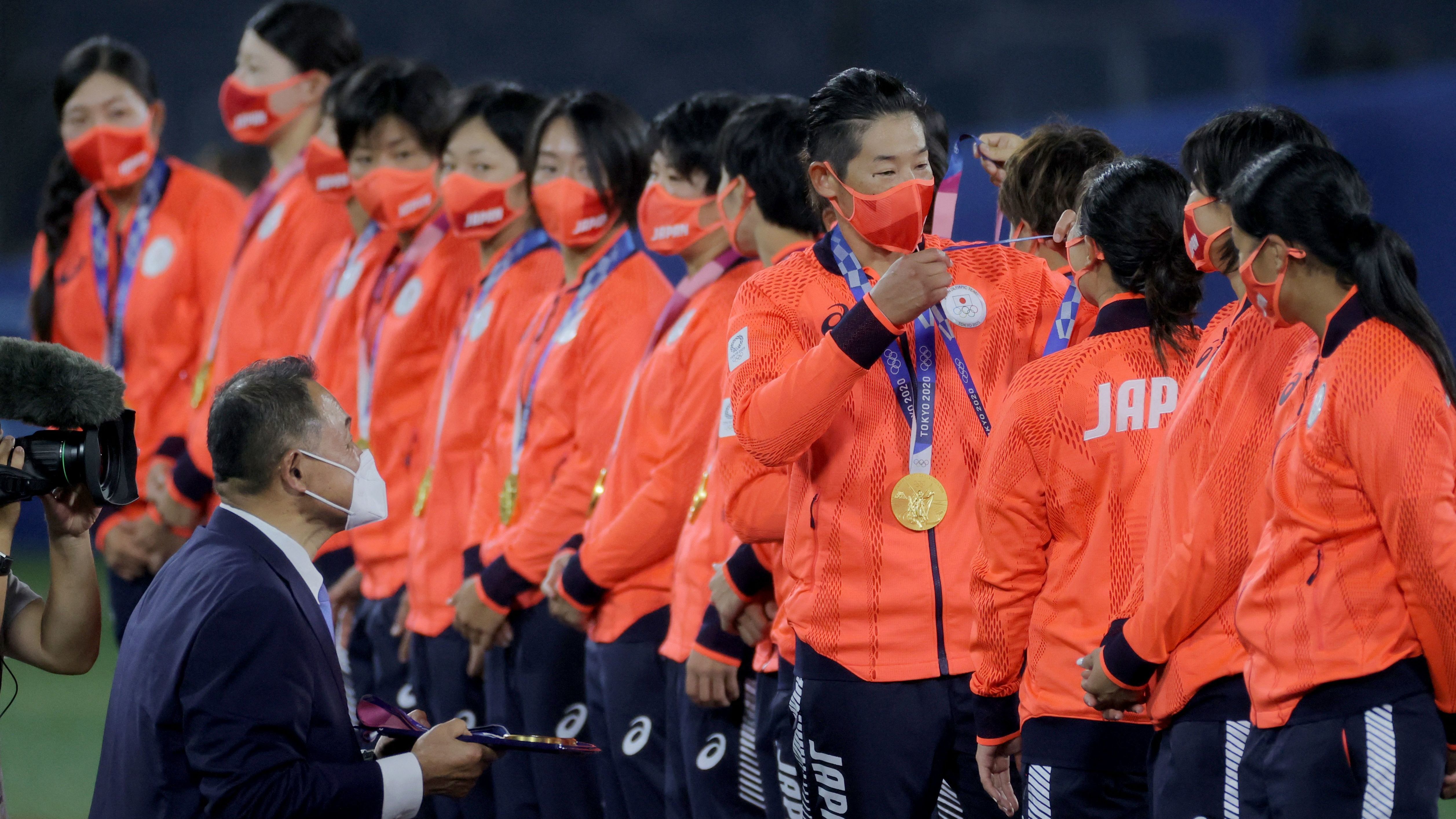 Japan's softball team watches player Yukiko Ueno (fourth from right) place a gold medal on catcher Haruka Agatsuma (third from right) on Tuesday. Japanese Olympic Committee President Yasuhiro Yamashita (lower left) holds the tray during the medal ceremony at the Yokohama Baseball Stadium in Yokohama, Japan.