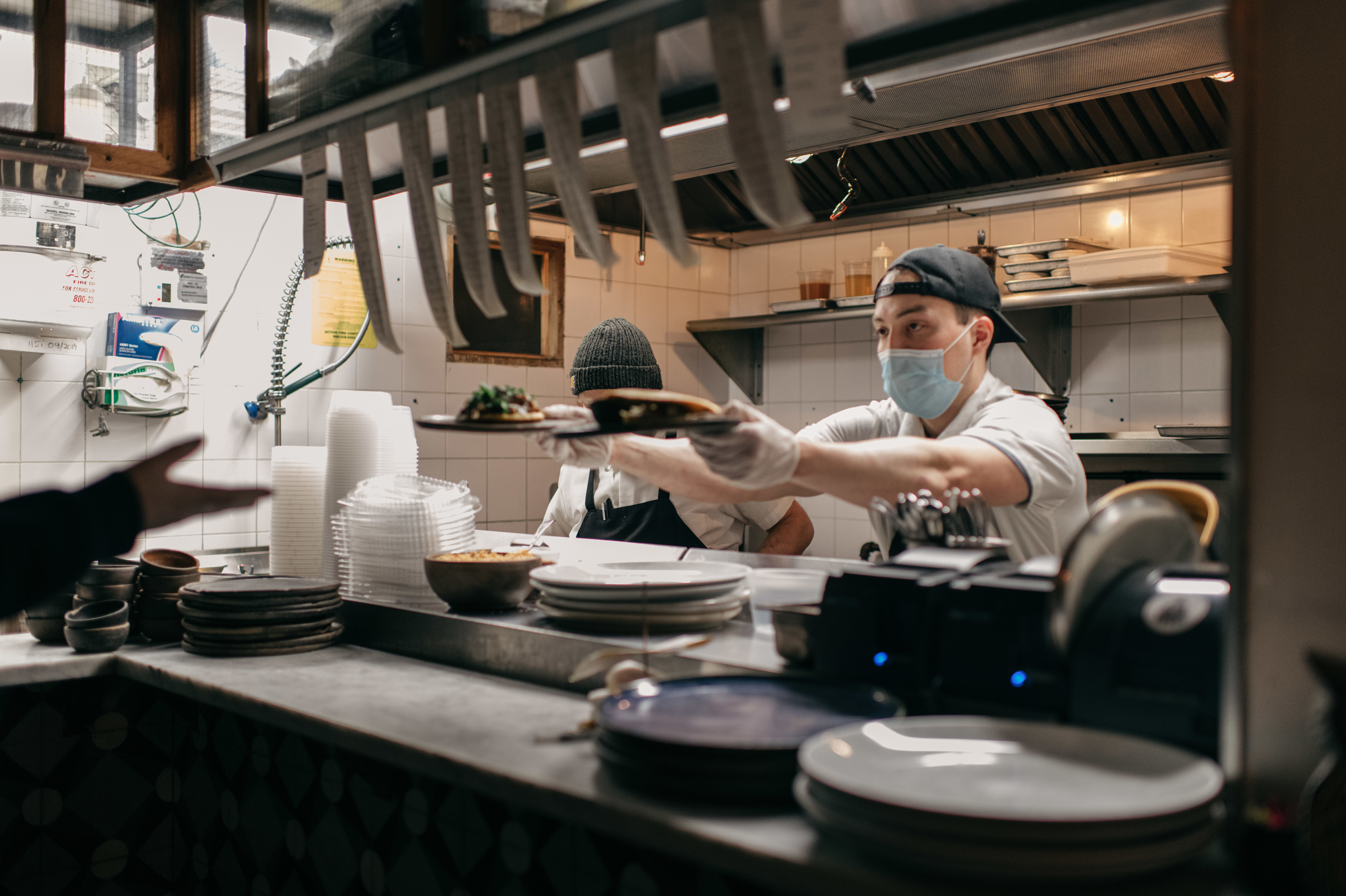 Masked kitchen workers pass plates of food to a server at Claro restaurant in February in New York City. Starting next month, those plates will go only to indoor diners who can prove they have been vaccinated. (Getty Images)