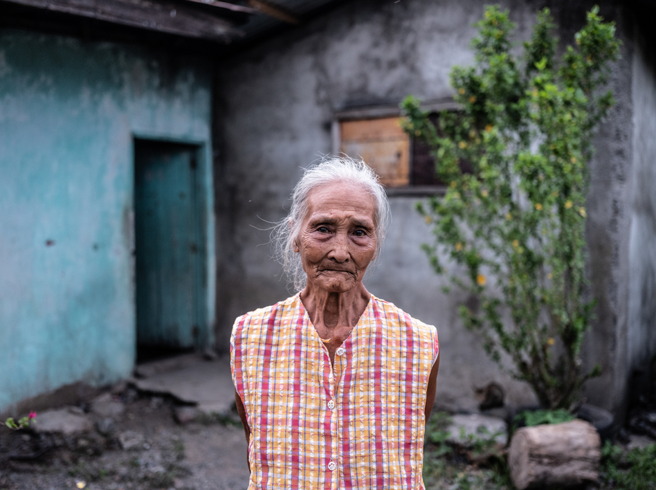 Gloria Hernandez, 82, stands outside her home in Aliaga, a village in the Philippines, where she lives with her daughter and grandsons. During the pandemic, she has been struggling to afford fresh meat and fish. (Xyza Cruz Bacani for NPR)