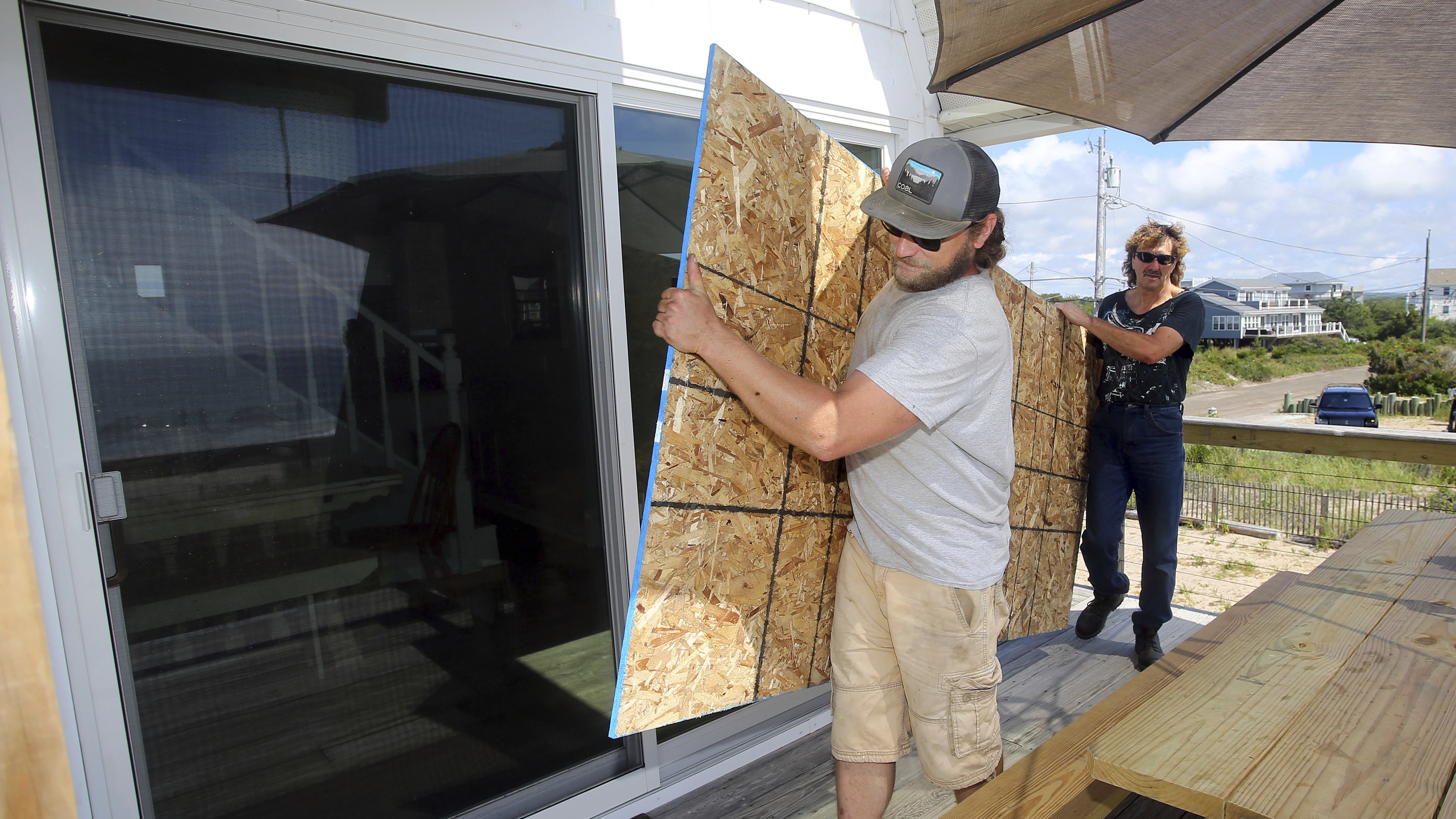 James Masog (center) and Gary Tavares prepare to board up a house Saturday in Charlestown, R.I., ahead of Hurricane Henri.