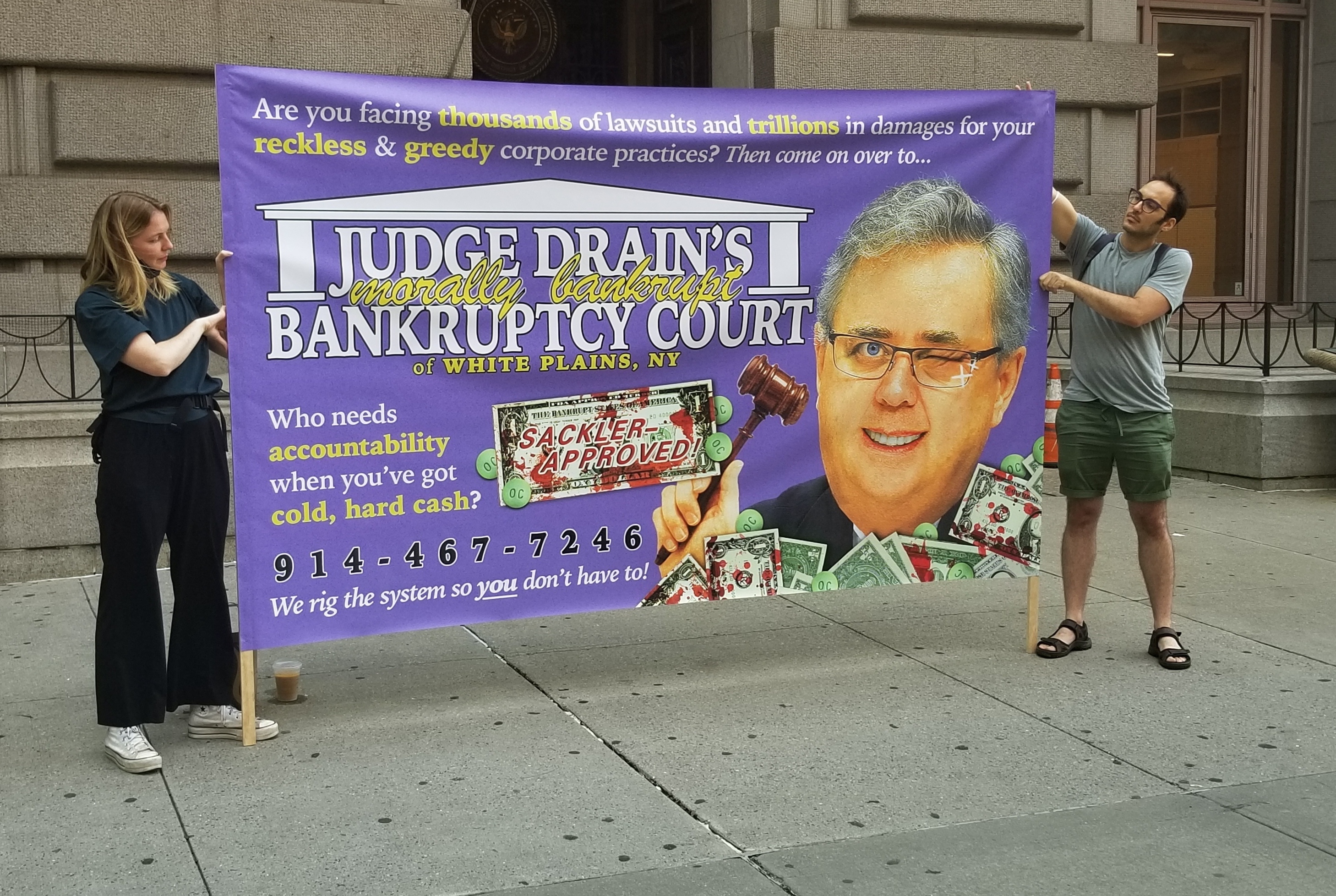 Two demonstrators protest against U.S. Judge Robert Drain, who has granted immunity from future opioid lawsuits to members of the Sackler family. (Brian Mann)