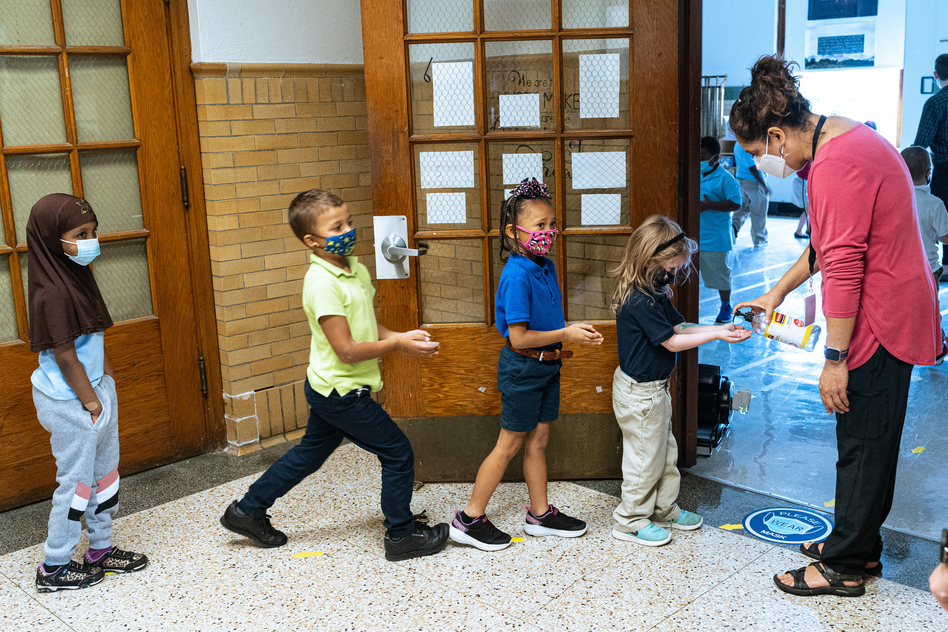 Quesada greets her second grade music class and gives them each a squirt of hand sanitizer as they enter her classroom.