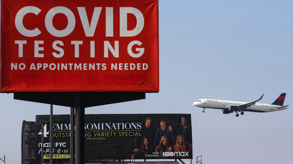 A Delta Air Lines plane lands near a COVID-19 testing sign at Los Angeles International Airport (LAX) on Aug. 25. Delta is increasing health insurance premiums for employees who are unvaccinated by $200 per month to cover higher costs of COVID-related care. The airline industry hasn't come out against a government-imposed vaccine mandate for domestic travel.