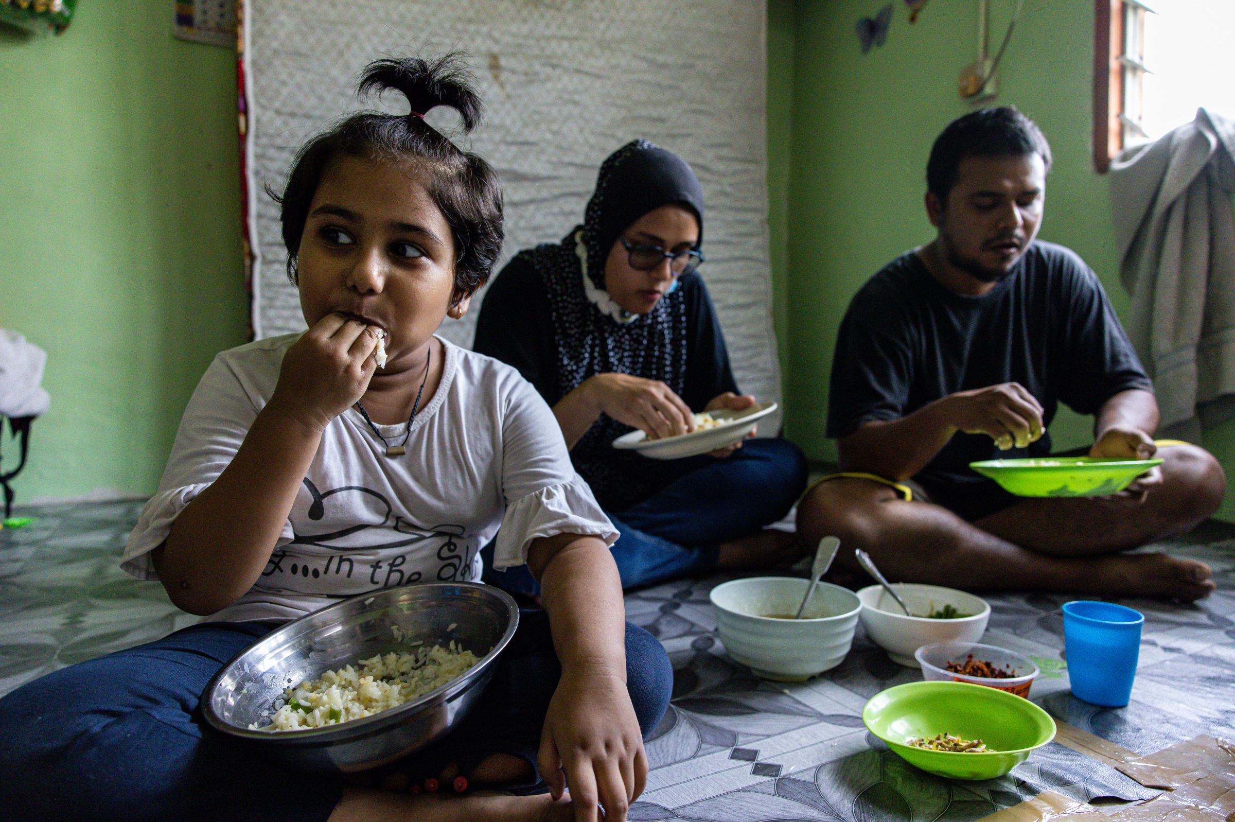 Mohd Ali, right, of Selangor, Malaysia, lost his job due to the pandemic. The family's favorite foods — fried chicken, eggs, fruit and bread — are now typically out of reach. When they can afford chicken, they give most of it to their daughter, Hosna. (Annice Lyn for NPR)