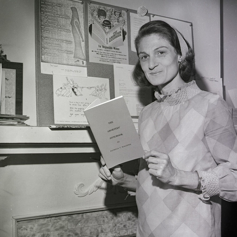 Patricia Maginnis holds her <em>Abortees' Songbook</em> and stands next to a bulletin board full of abortion information. The early abortion rights advocate, pictured here in 1970, died earlier this year. (Bettmann Archive)