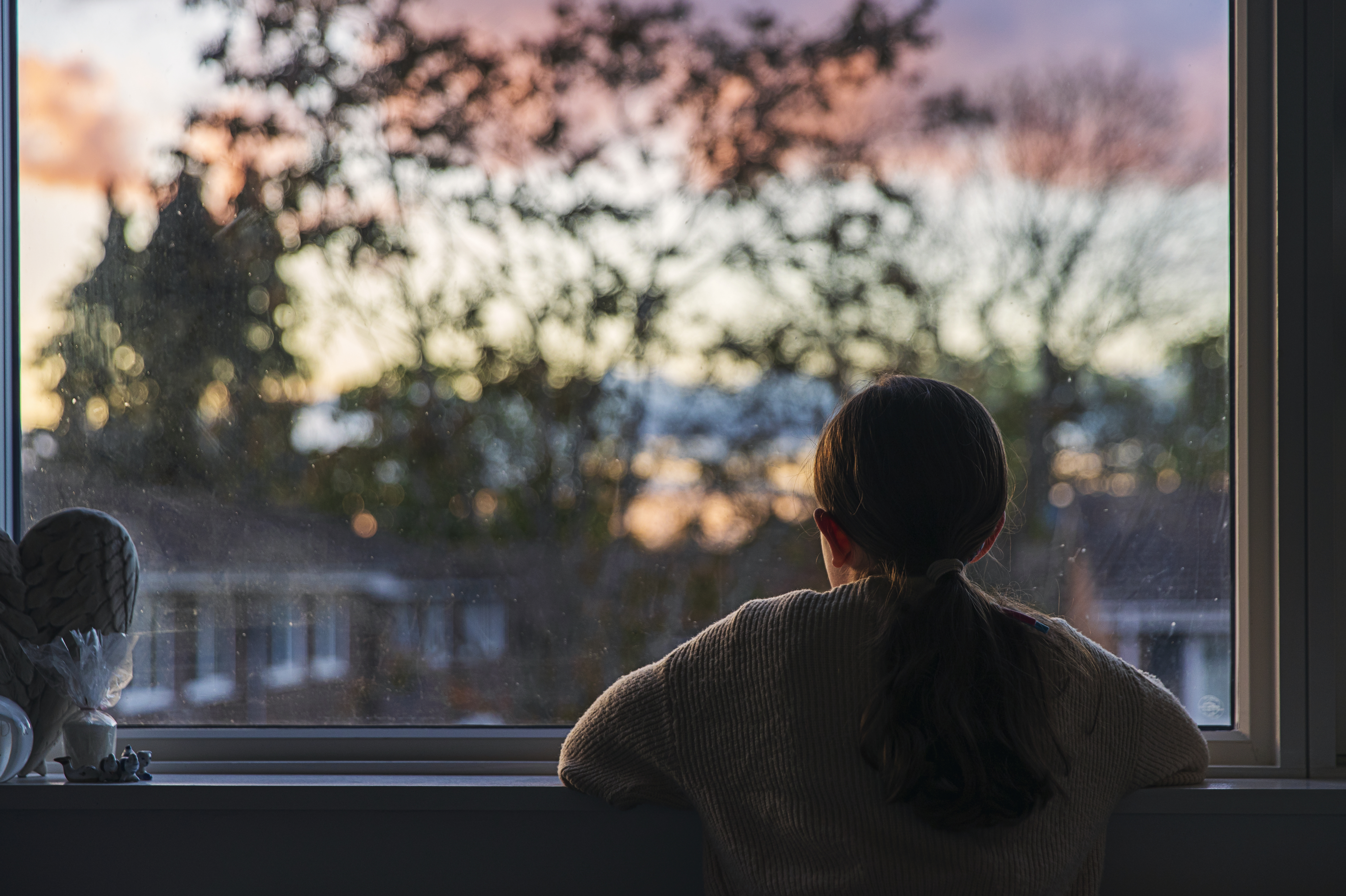 A girl looks out of her bedroom window as the sun is setting. (Getty Images)