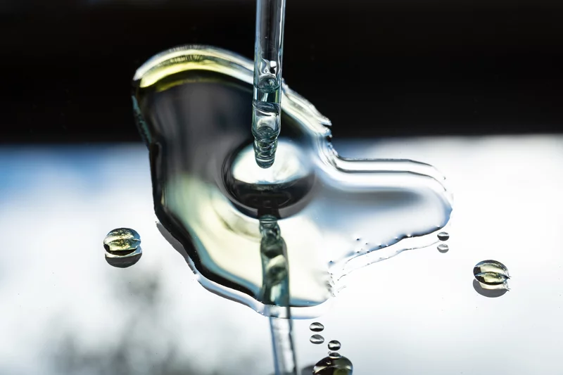 A photograph that shows a dropper releasing a drop of serum into a small dollop of serum on a mirror.