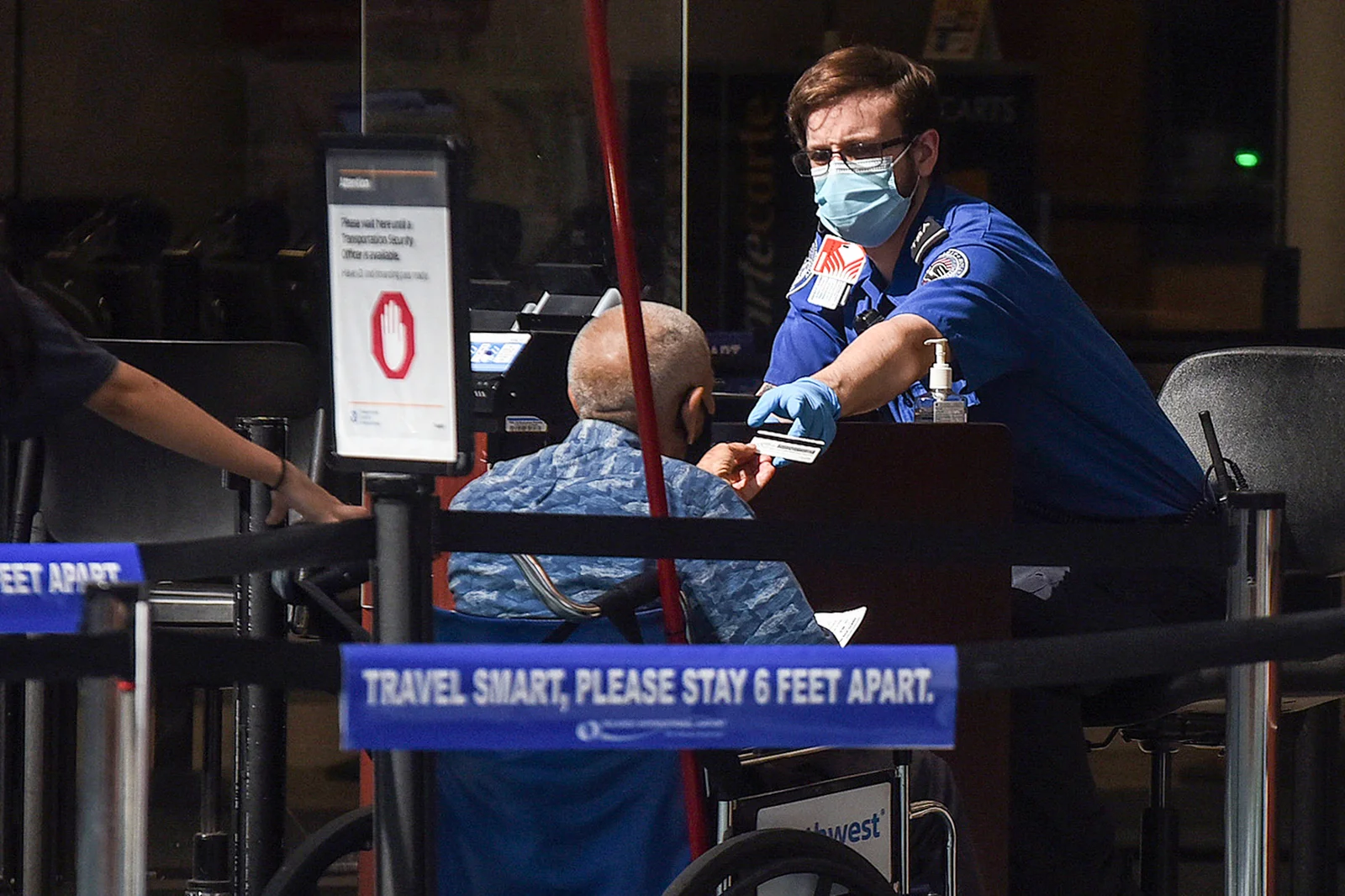 A man using a wheelchair hands his ID to an officer at a security screening checkpoint at Orlando International Airport in 2020