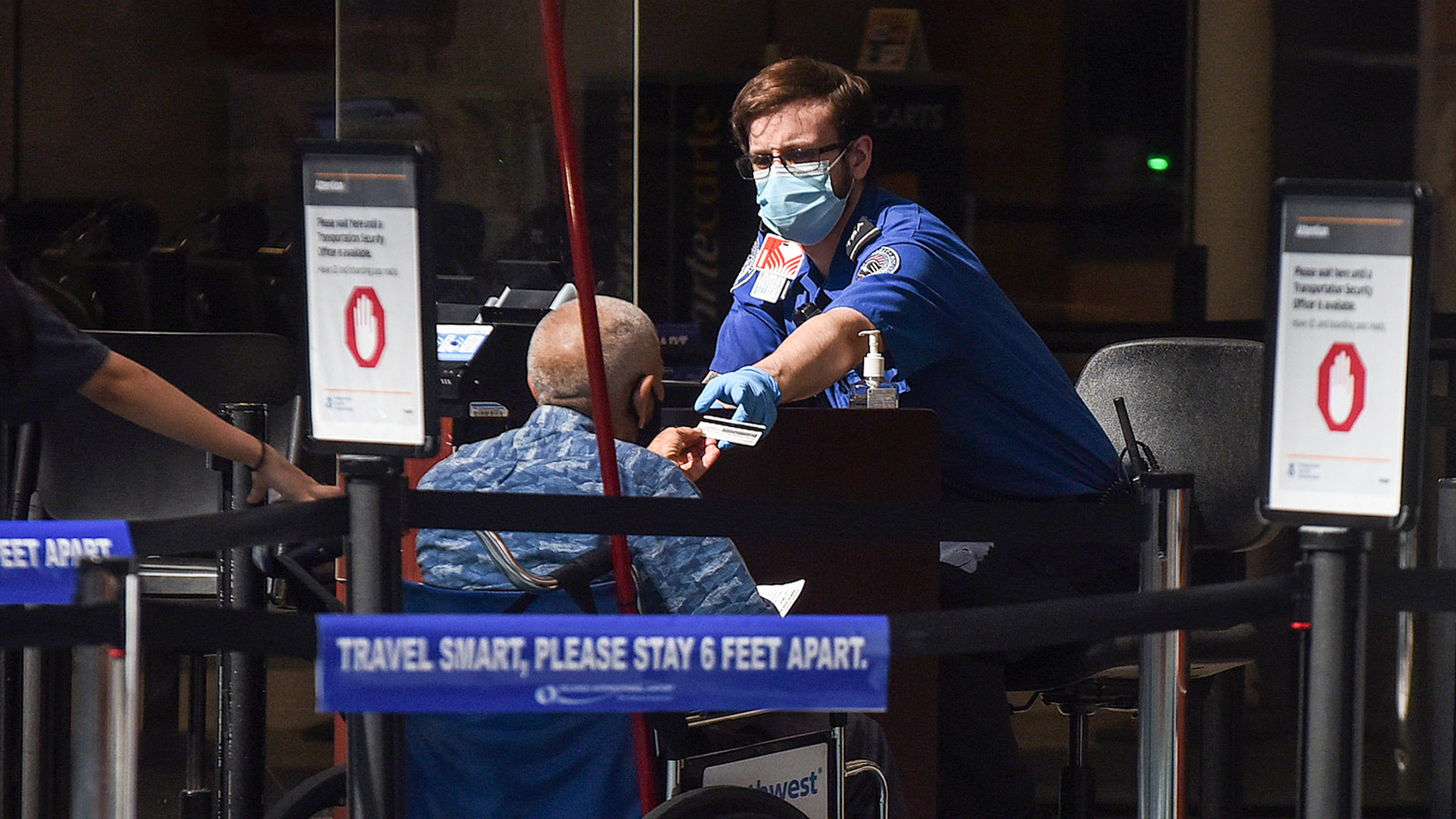 A man using a wheelchair hands his ID to an officer at a security screening checkpoint at Orlando International Airport in 2020.