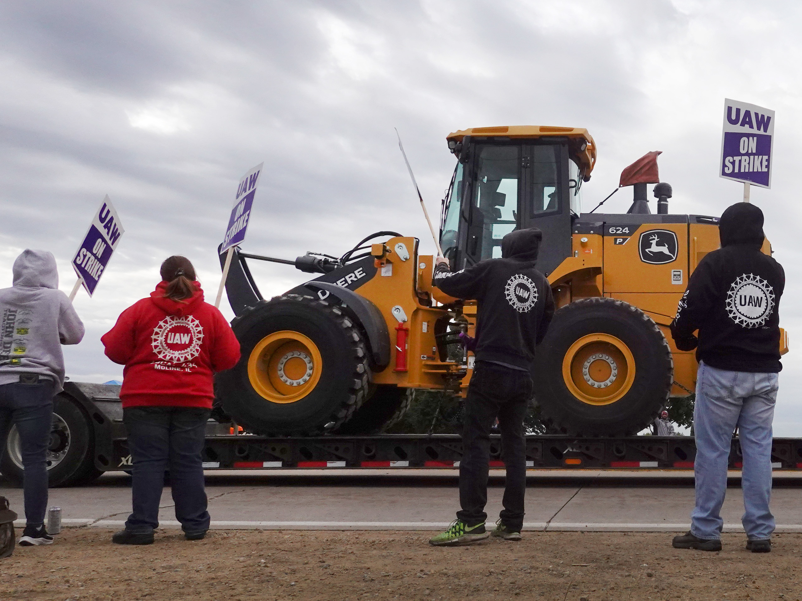 A truck hauls a piece of John Deere equipment from the factory past workers picketing outside the John Deere Davenport Works facility on Oct. 15 in Davenport, Iowa. More than 10,000 John Deere employees, represented by the UAW, walked off the job in mid-October after failing to agree to the terms of a new contract. (Getty Images)